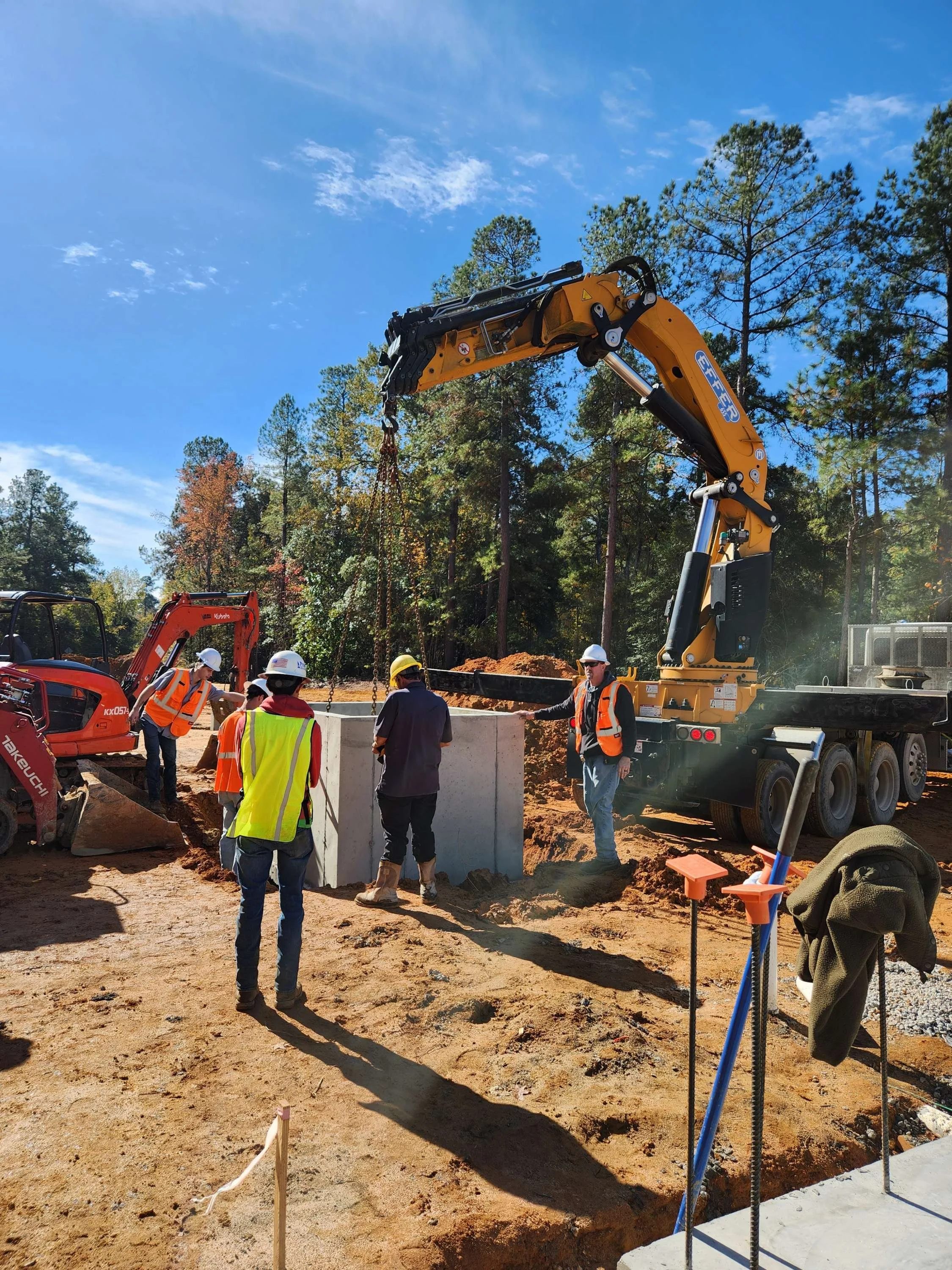 Construction workers and equipment at a construction site with a large crane and a concrete foundation