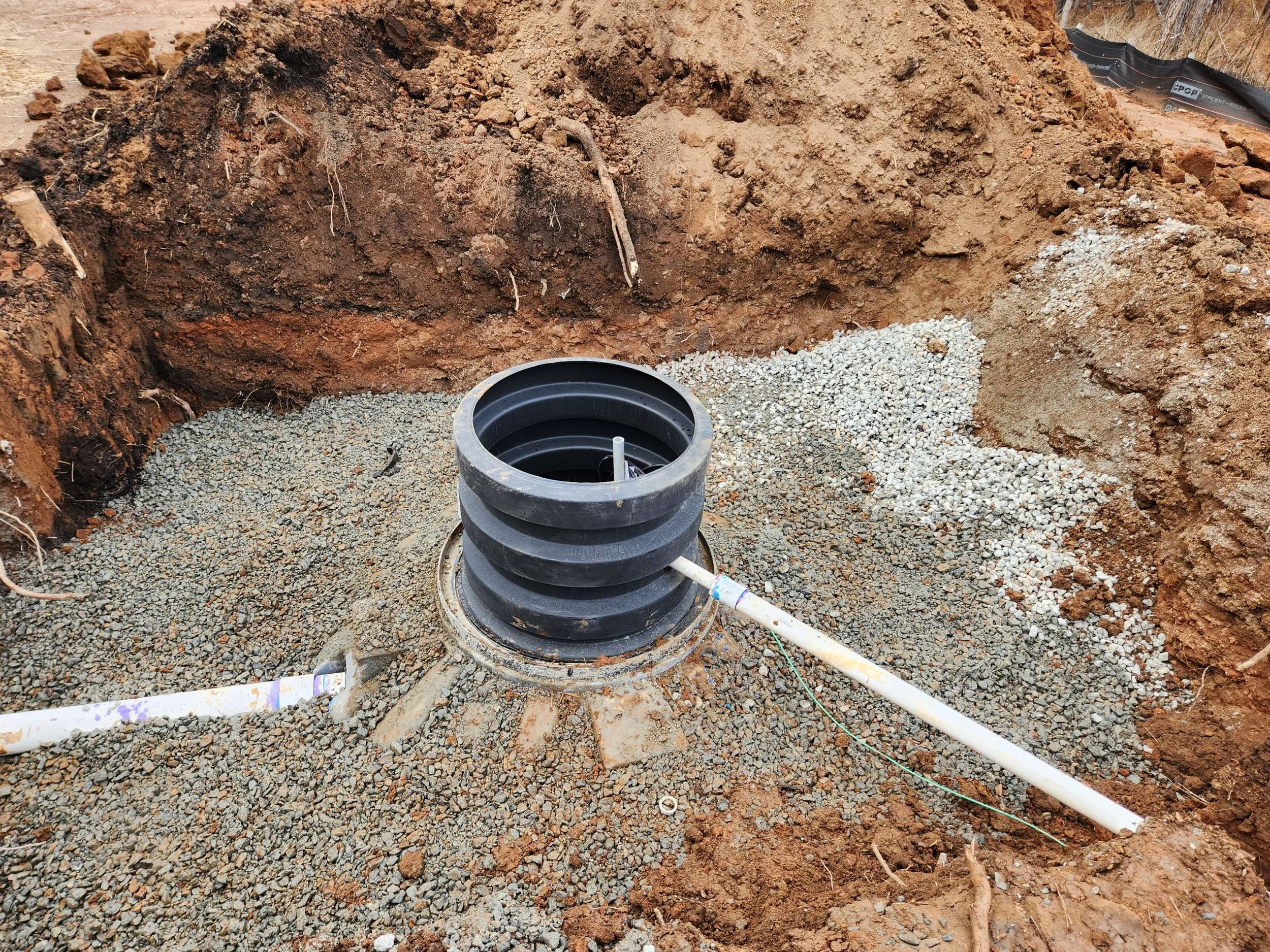 Underground plumbing installation with black coupling and white pipes in a dirt excavation site.