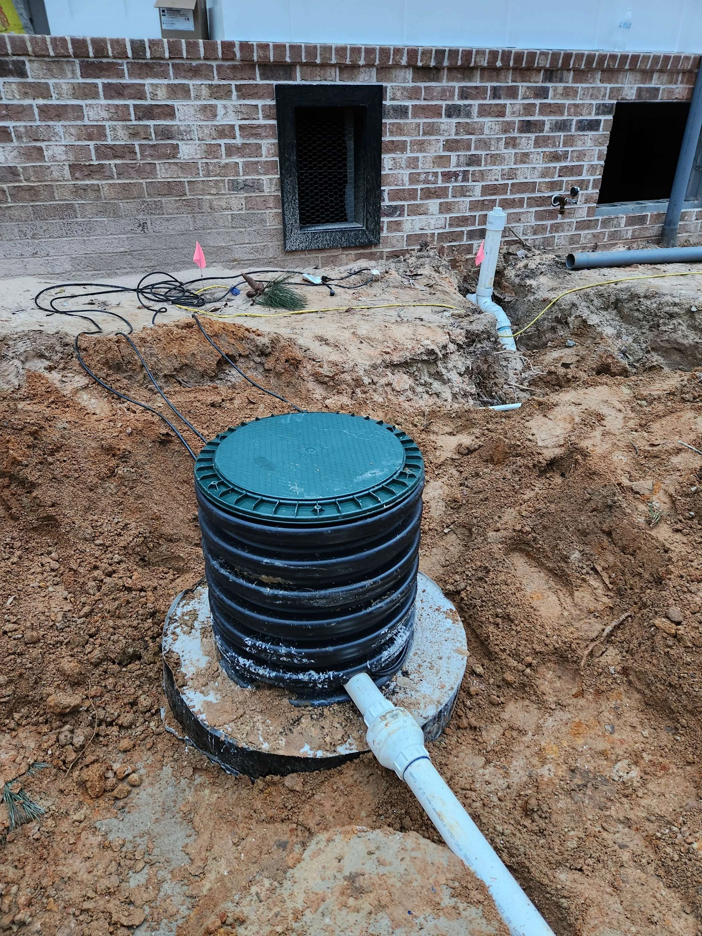 Underground installation of a septic tank or similar system with pipes, dirt, and construction markers.