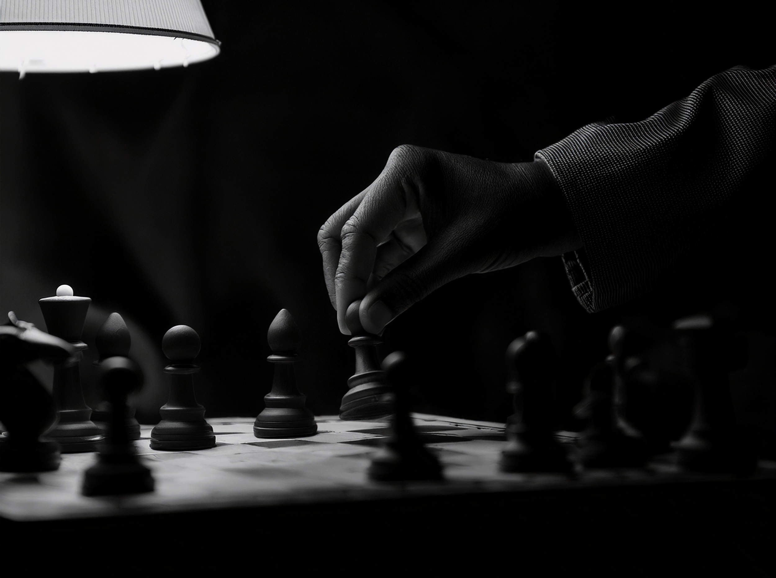 A person making a move in a chess game, captured in black and white with a dark background.