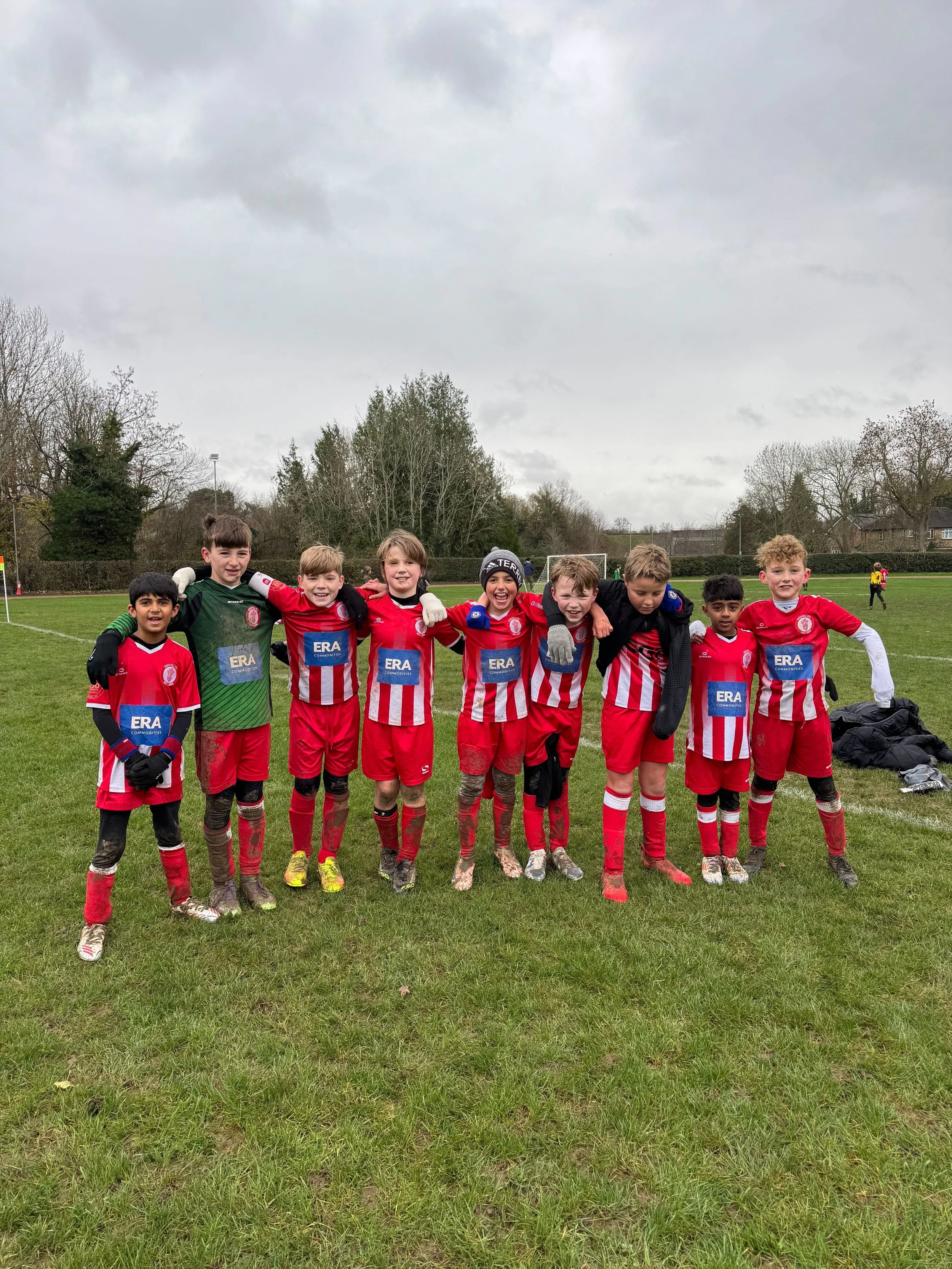 Children in football kit standing together on a field after a game, with arms around each other.