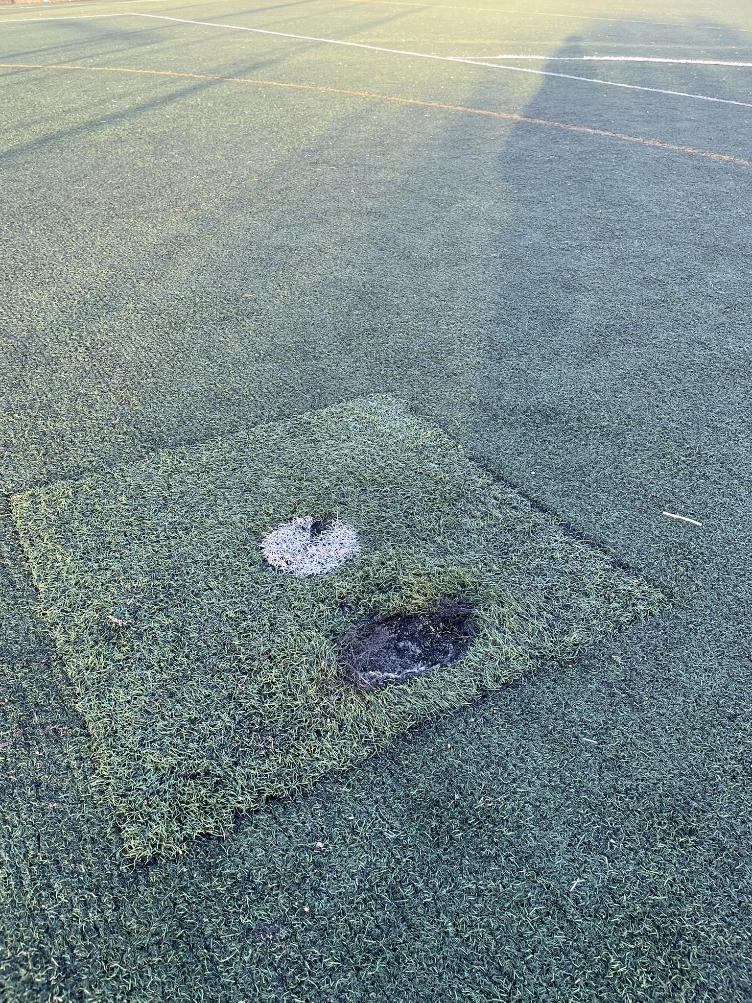Close-up of a green sports field with two circular patches of worn grass—one with white chalk or paint and the other darker and damaged.
