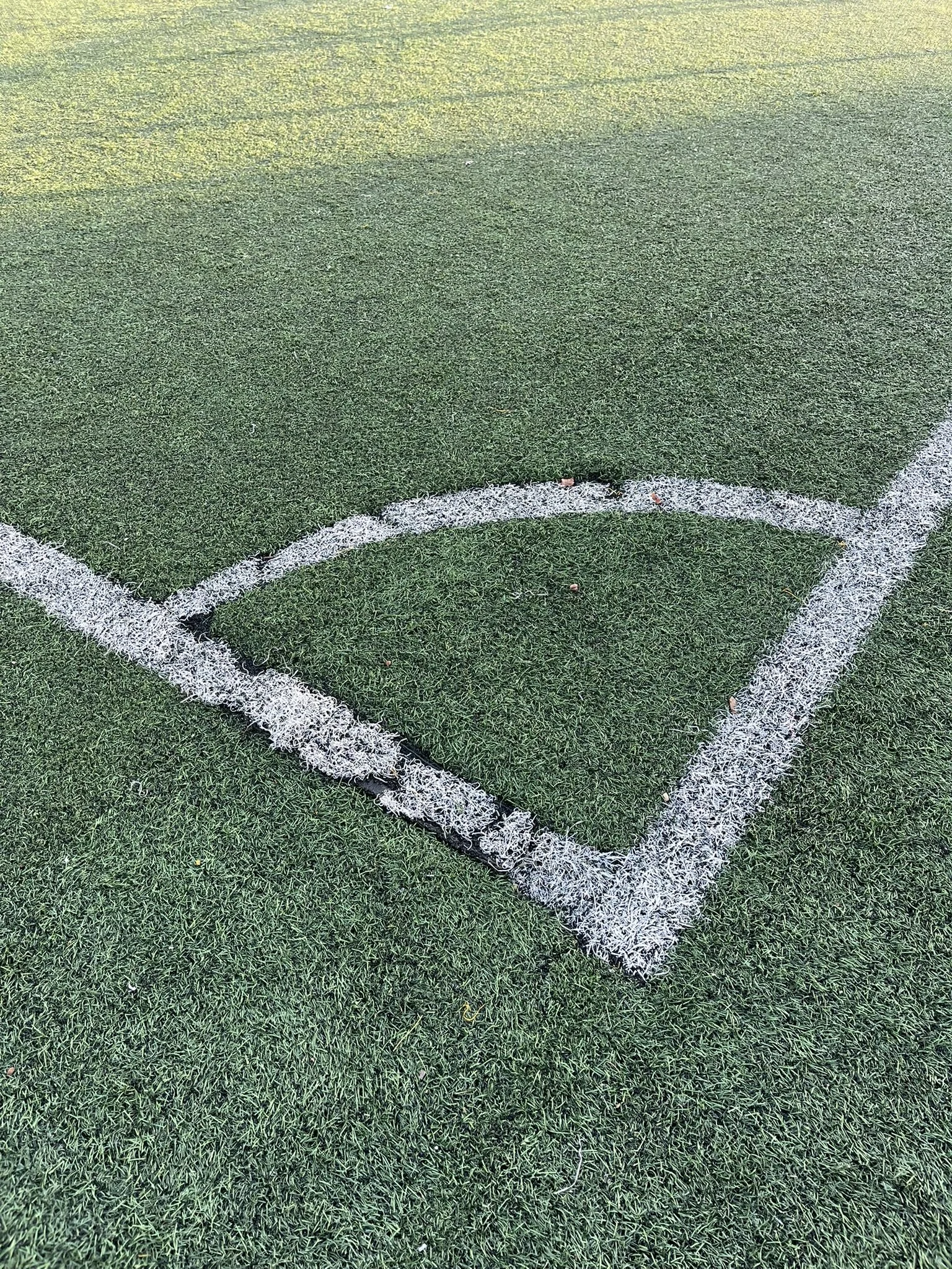 Close-up of a sports field corner with white boundary and goal area lines on green artificial turf.