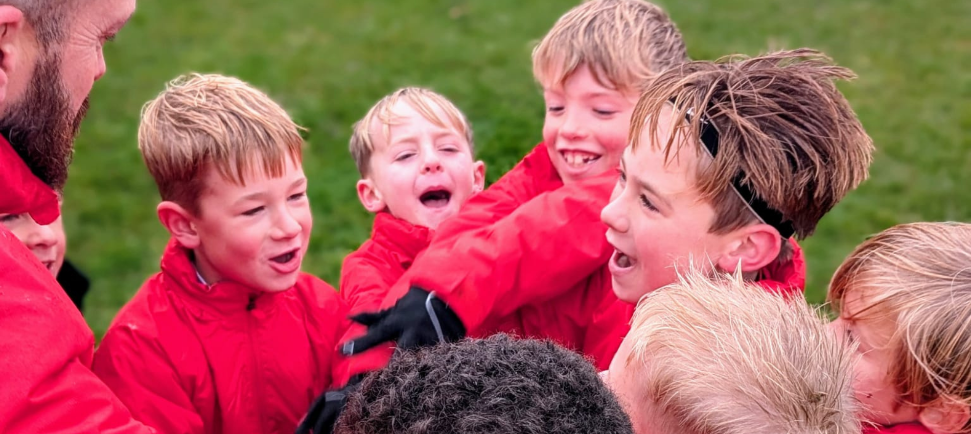 Children in red jackets celebrating outdoors, hugging and smiling.
