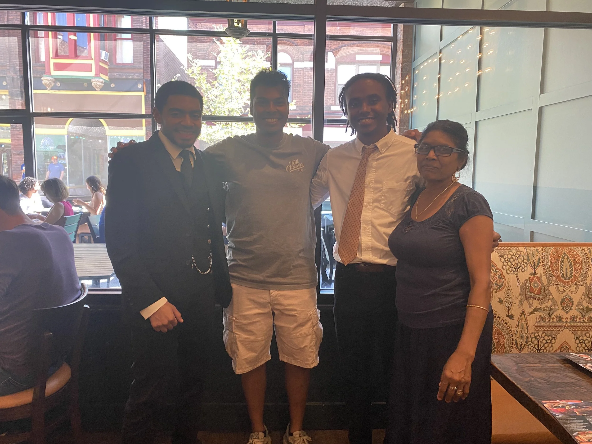 Four people standing together inside a restaurant near a large window, smiling and posing for a photo.