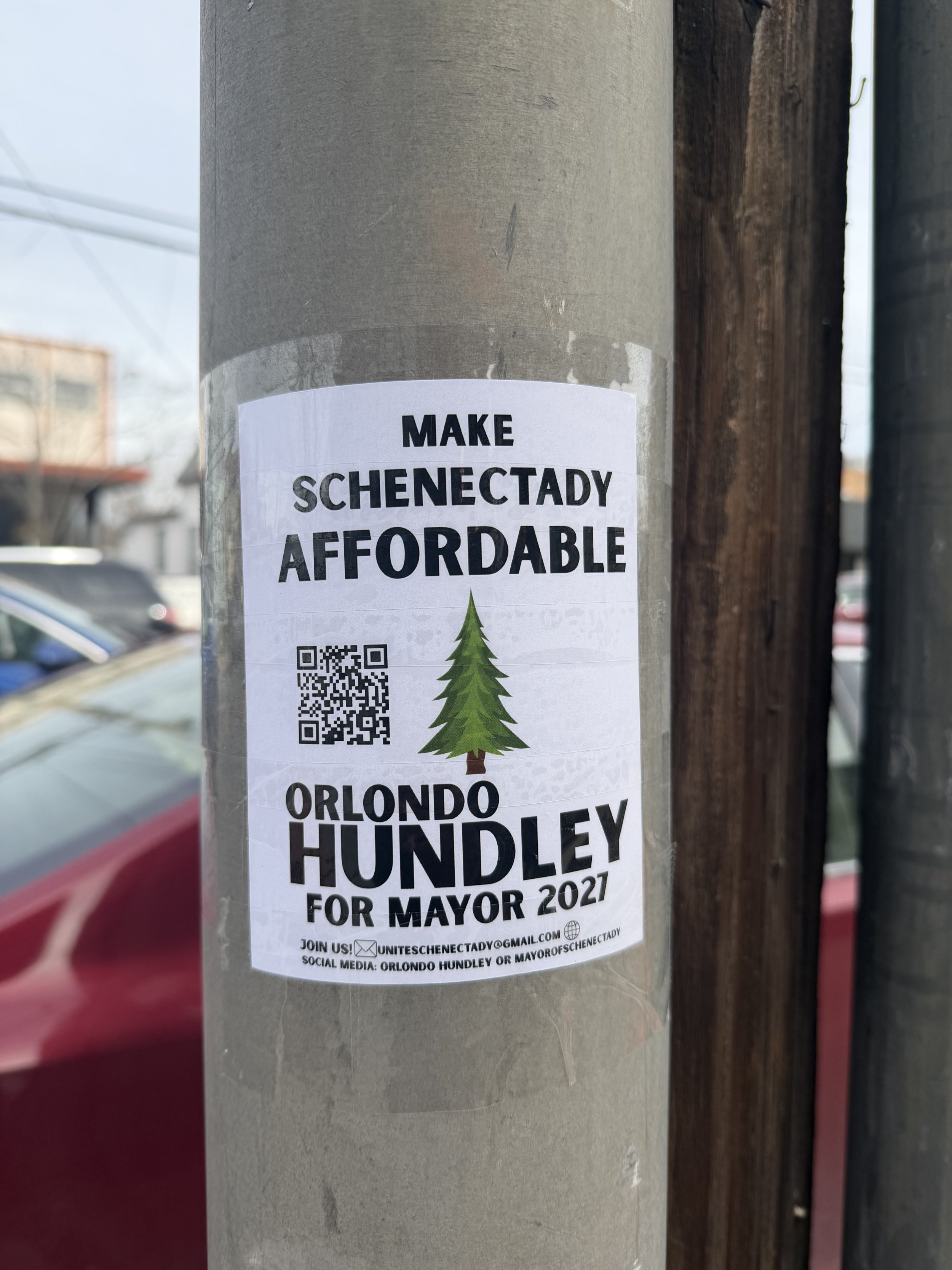Flyer on a pole encouraging people to make Schenectady affordable, featuring a QR code, a pine tree graphic, and promoting Orlondo Hundley's 2021 mayoral campaign.