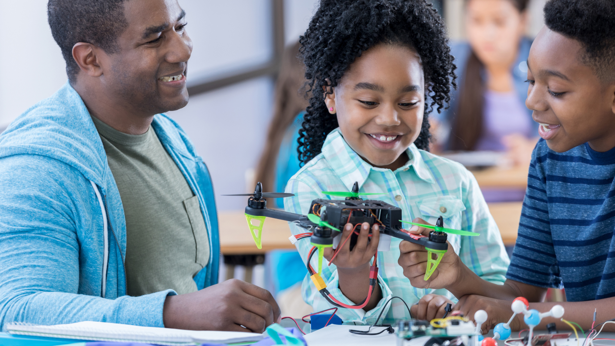 An adult male and two children working together on a drone project in a classroom.