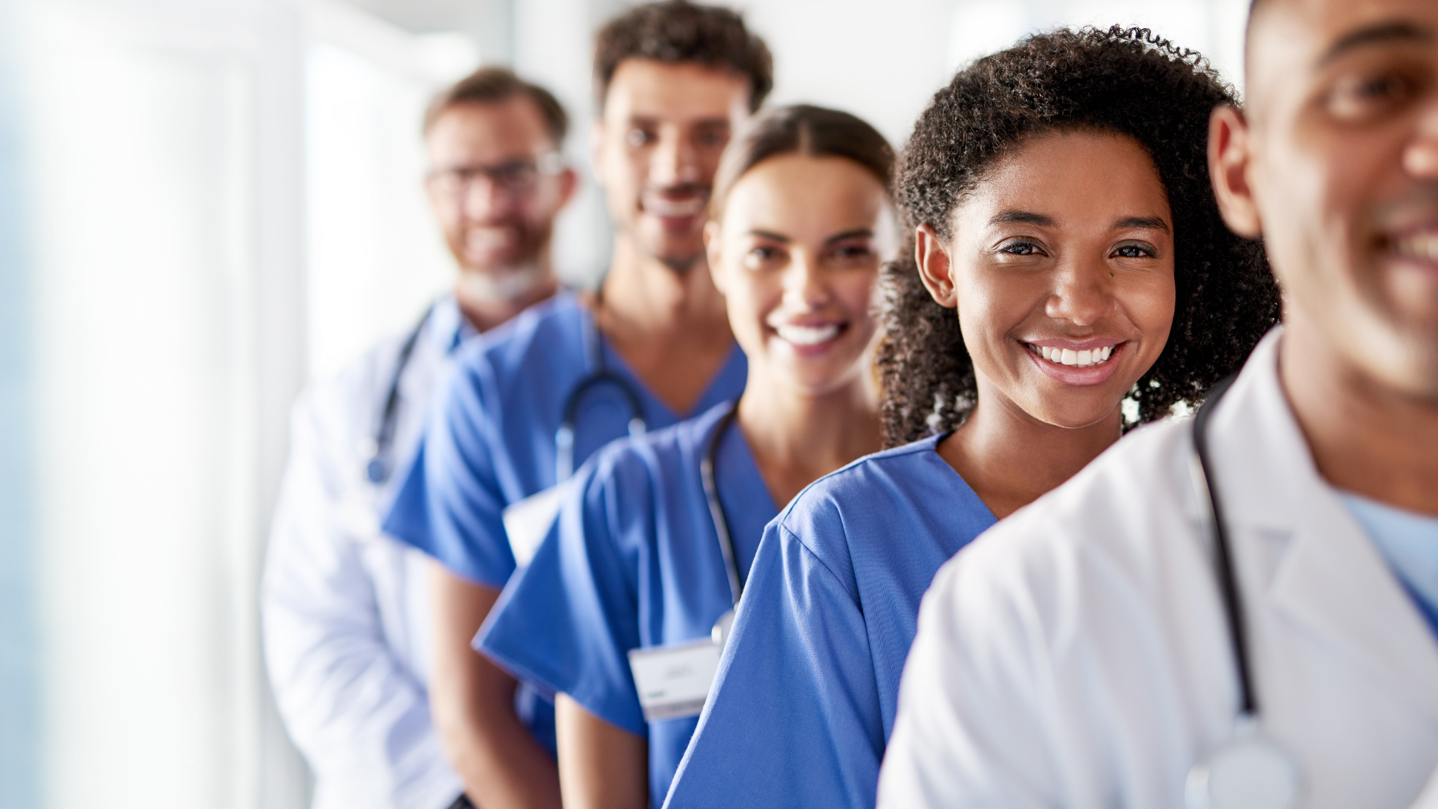 Line of healthcare professionals, including nurses and doctors, smiling and standing in a hospital corridor.