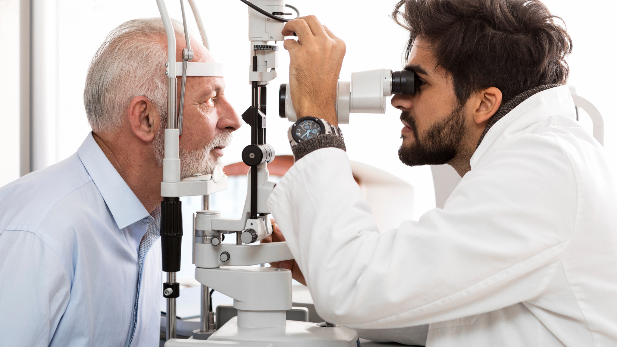 Optometrist performs eye examination on elderly man using a slit lamp device.