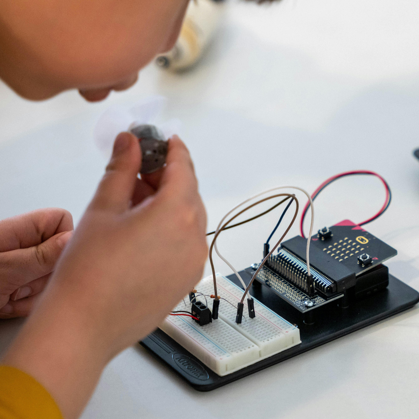Child working on an electronics project with a breadboard, microcontroller, and wires.