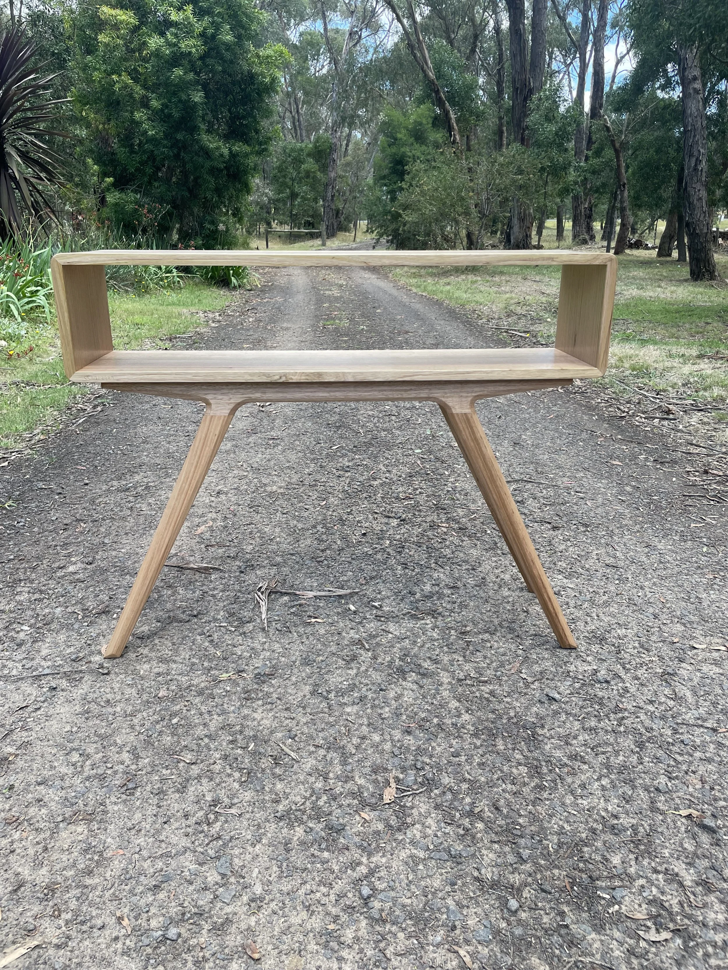 Wooden table with open rectangular frame design placed on a dirt road in a wooded outdoor setting.