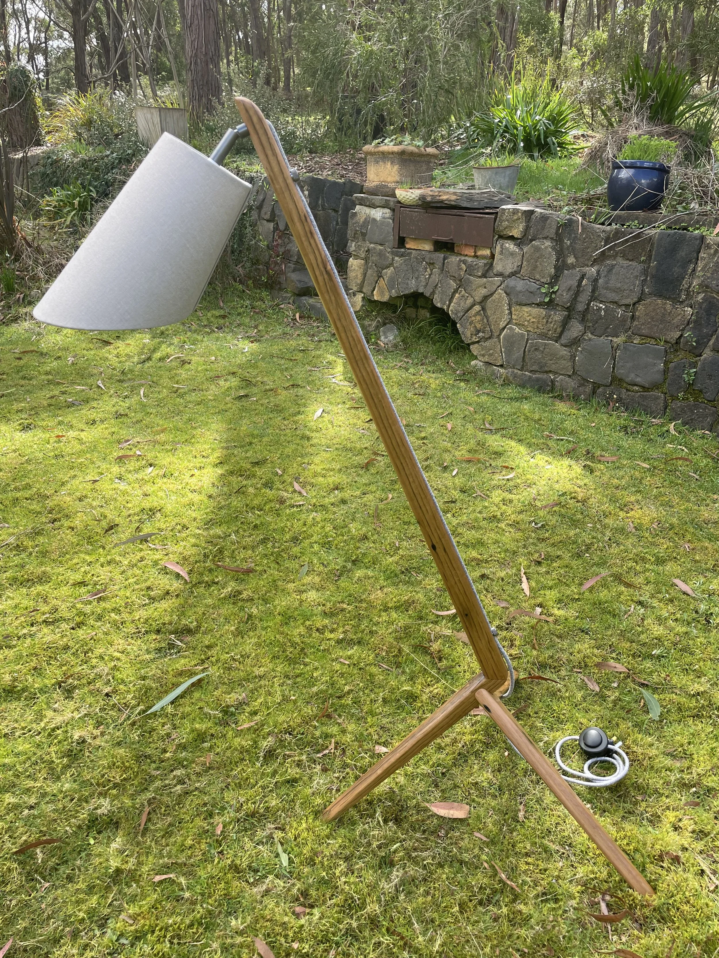 A modern wooden floor lamp with a curved neck and fabric shade standing on a grassy yard.