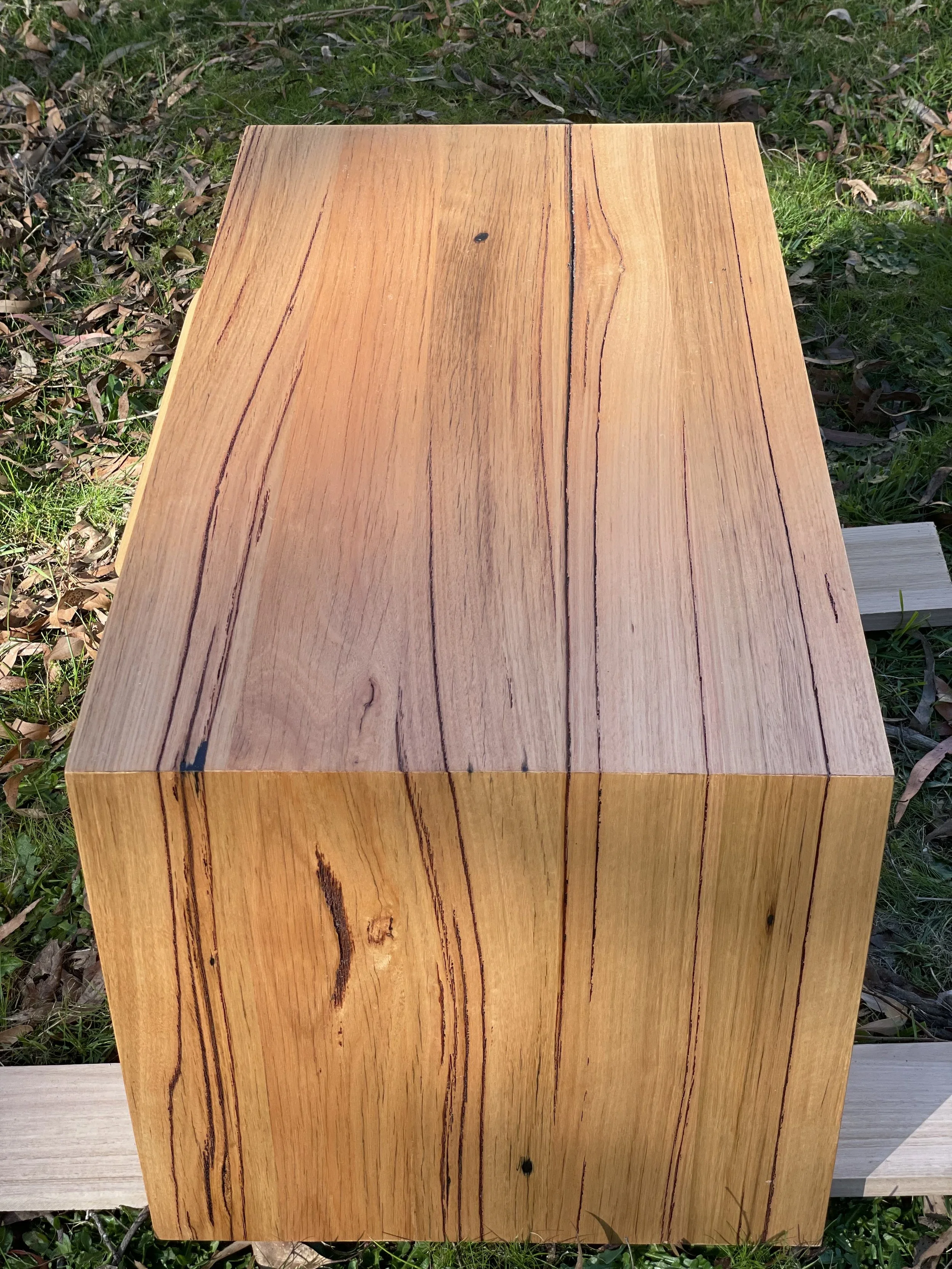 A rectangular wooden block with visible grain patterns on an outdoor grassy surface.