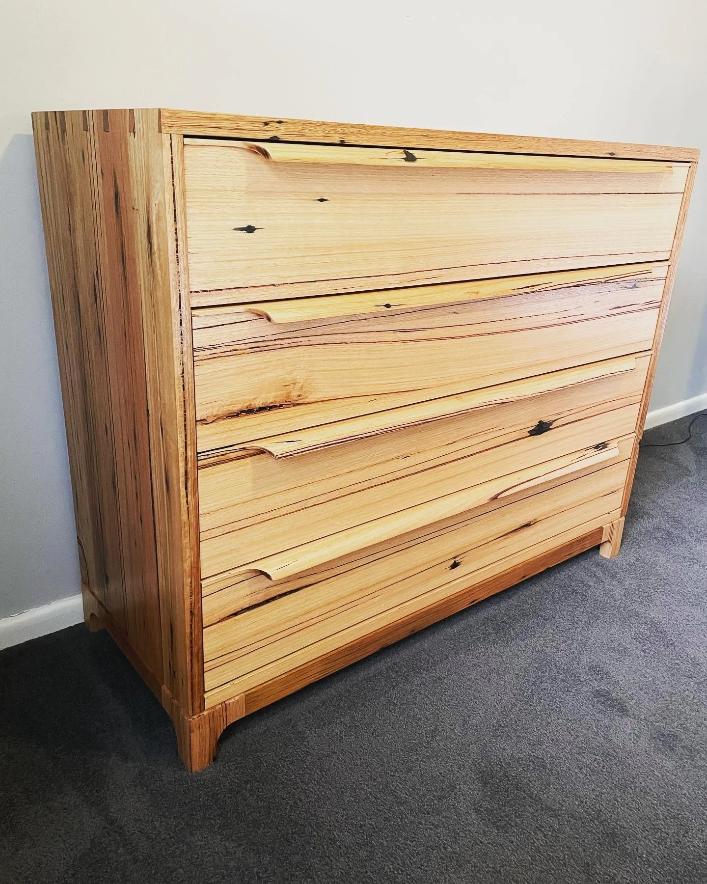 A wooden dresser with horizontal slats, natural wood finish, against a white wall and gray carpeted floor.
