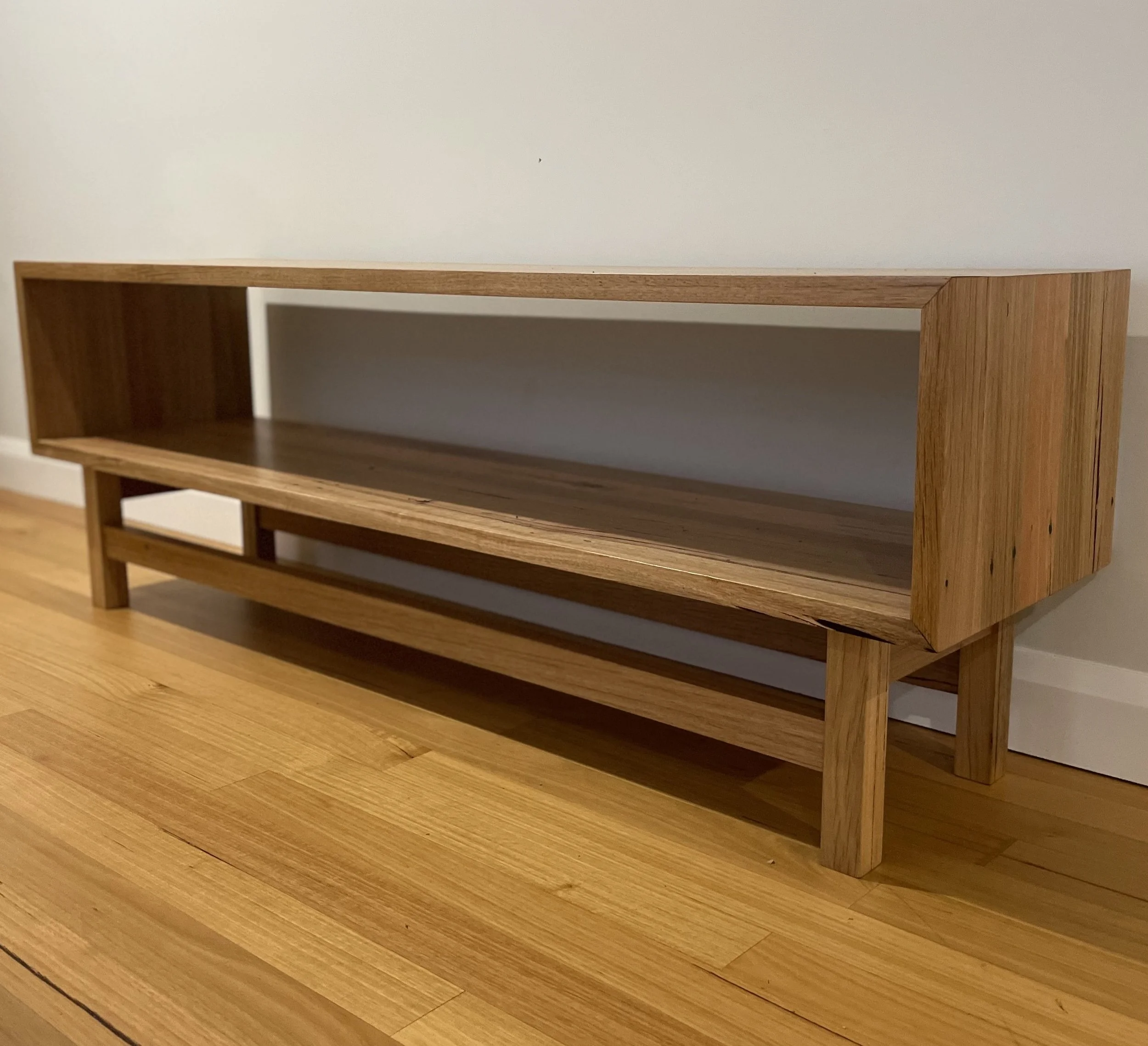 Wooden open shelf or console table with a lower shelf, placed on a wooden floor against a plain wall.