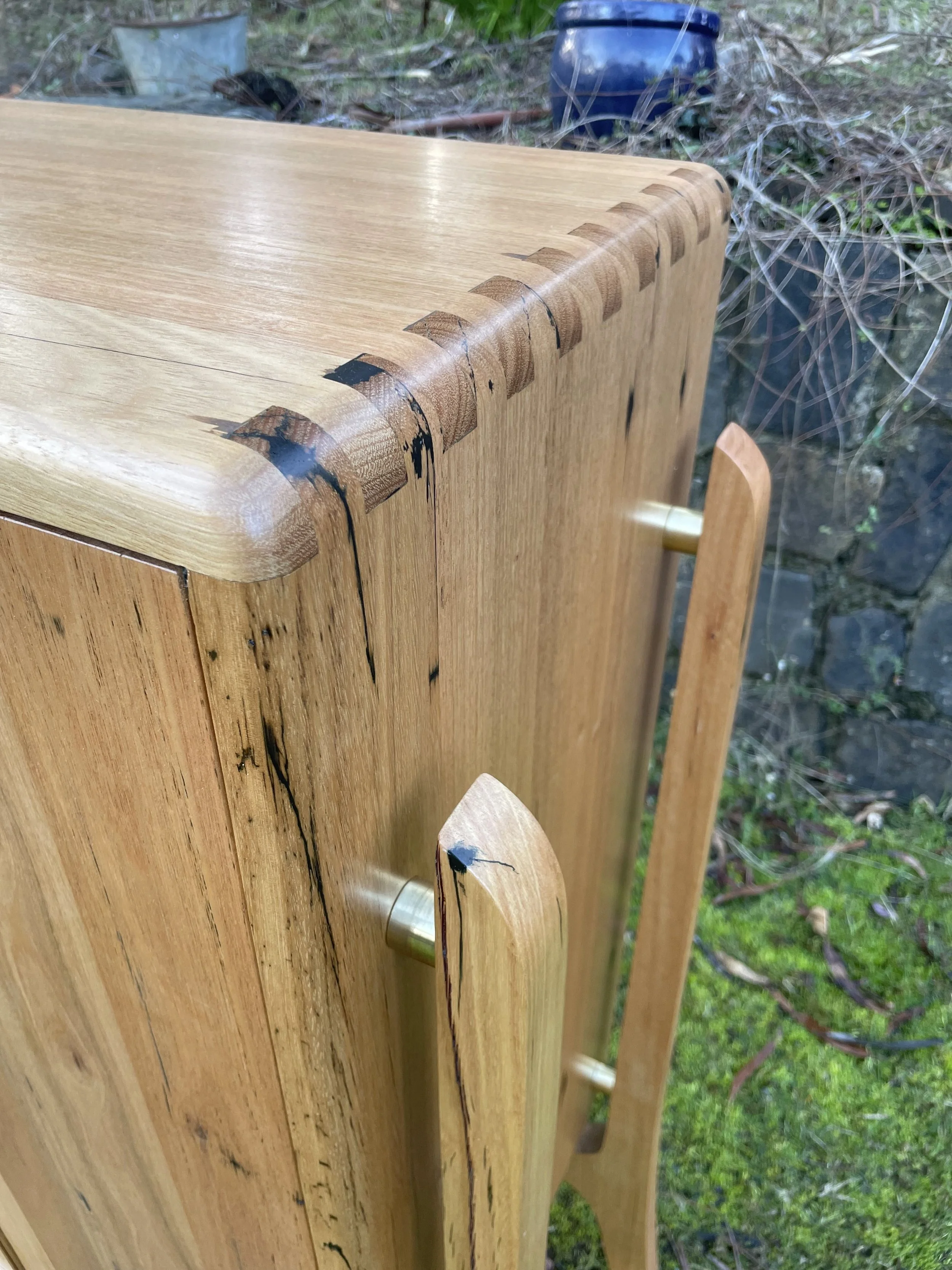 Close-up of a wooden cabinet with visible cracks and damage, outdoors with grass and rocks in the background.