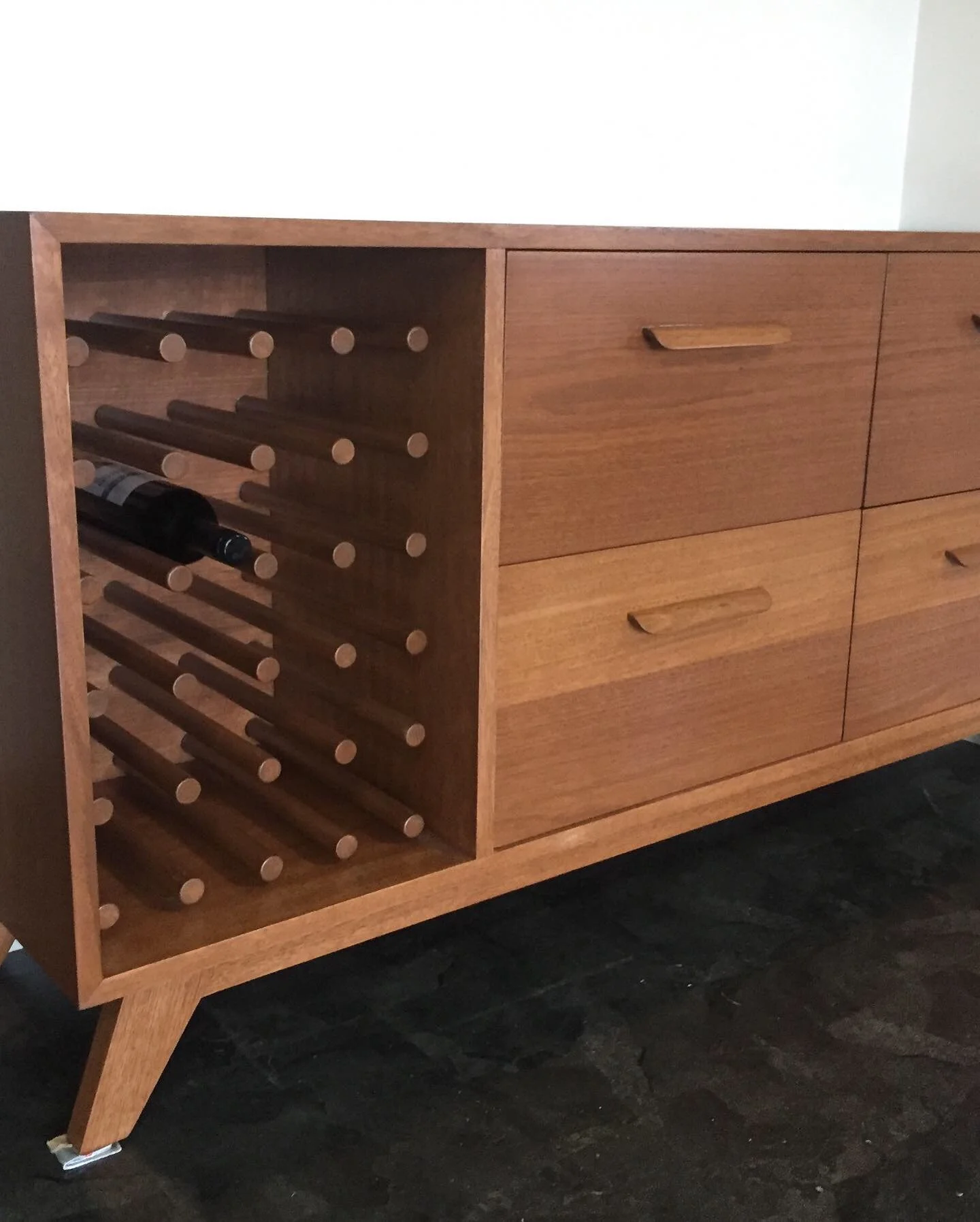 A wooden sideboard with a wine rack on the left and four drawers on the right.