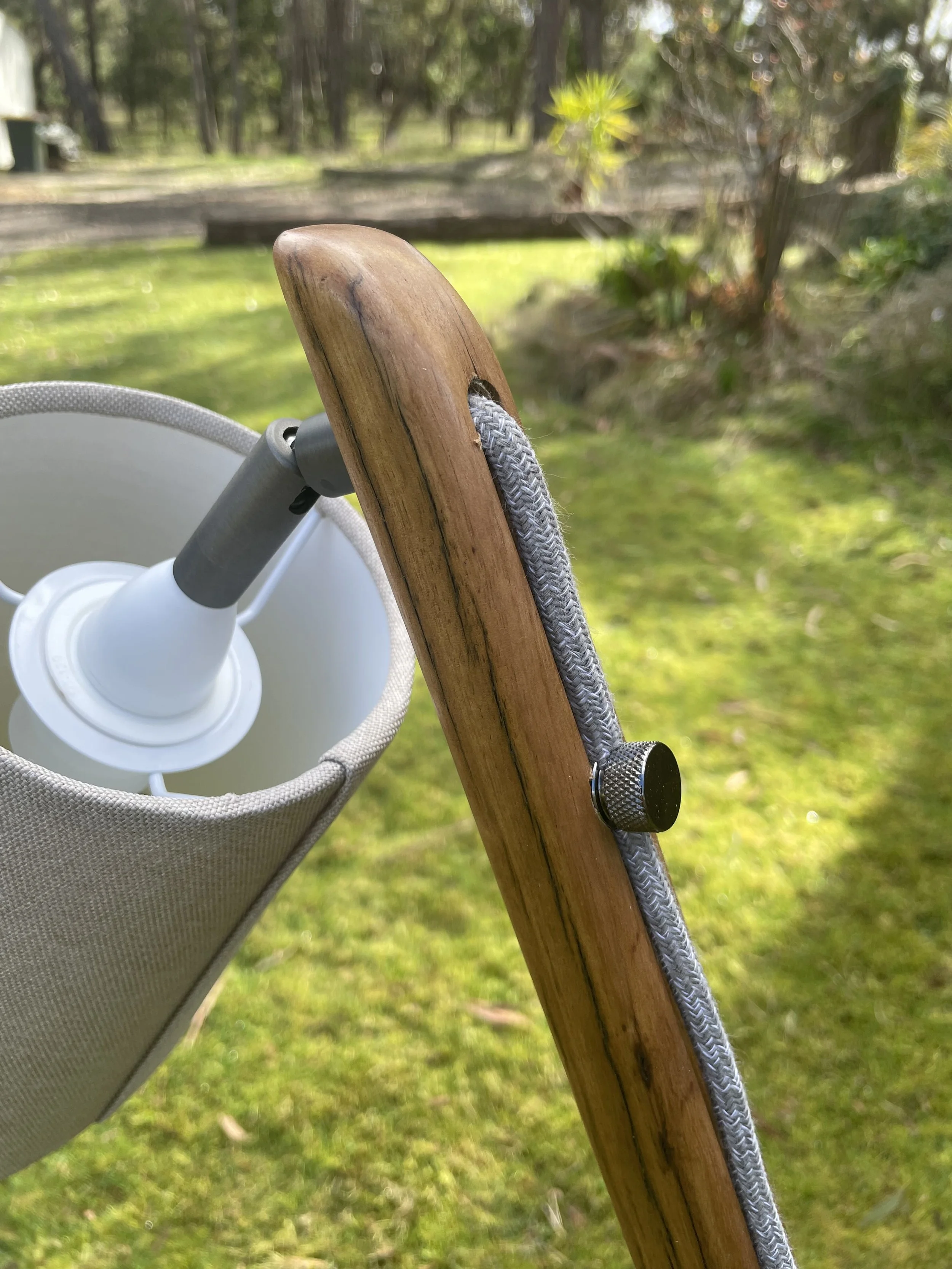 Close-up of a wooden chair with a gray rope wrapped around the backrest, outdoors on a grassy area with trees in the background.