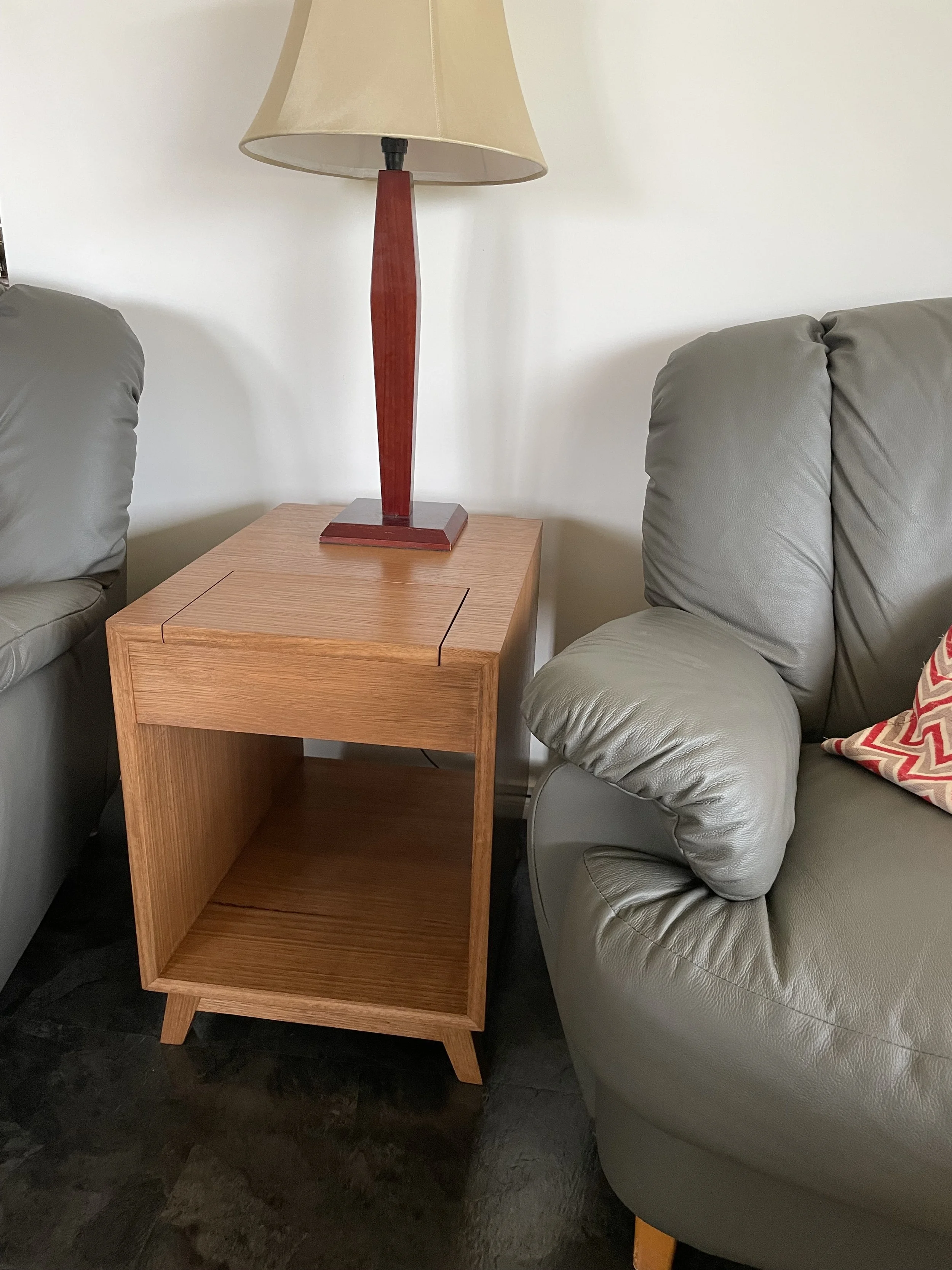 A wooden side table with a lamp on top, placed between two gray leather sofas in a living room.