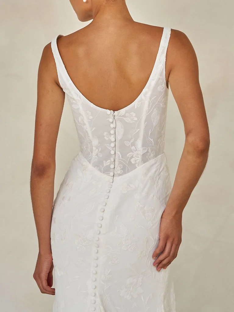 Madi Lane Wilcox minimalist fit-and-flare wedding dress with a scoop illusion bodice, embroidered tulle chiffon, Basque waist, asymmetrical draping, and leg split.