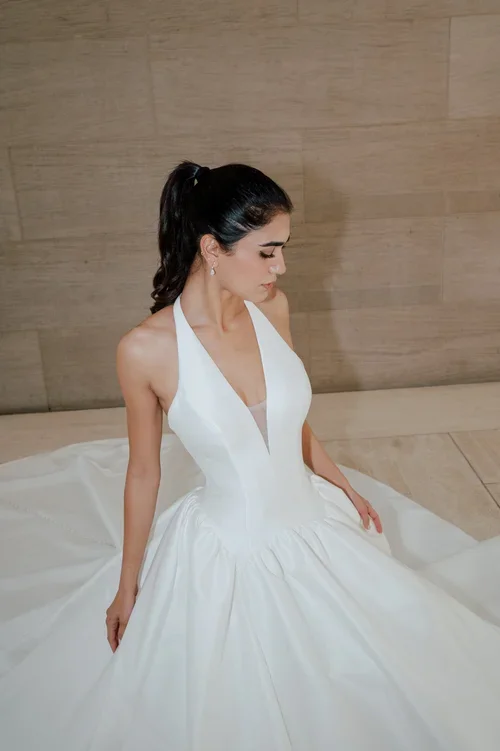 Elizabeth Lee Zoey satin ballgown with a halter plunging V-neckline, full skirt, and side pockets, available at Bride To Be Couture in Sacramento.