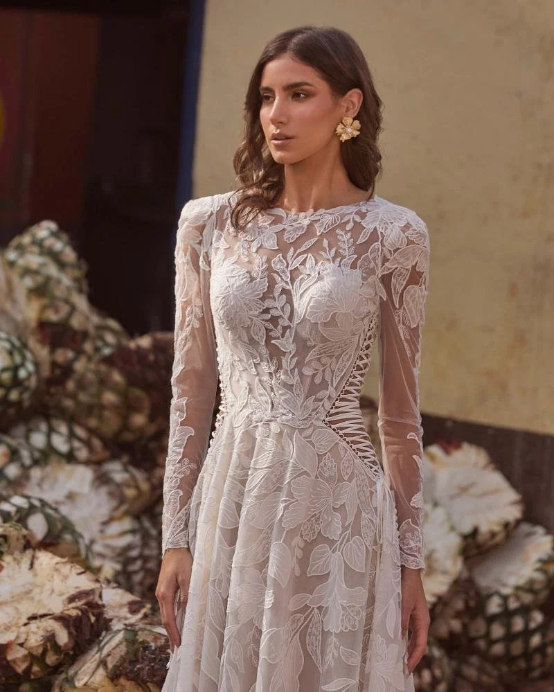 La Perle Gayle boho lace A-line wedding dress with high jewel illusion neckline, long lace sleeves, side cutouts, and low back.