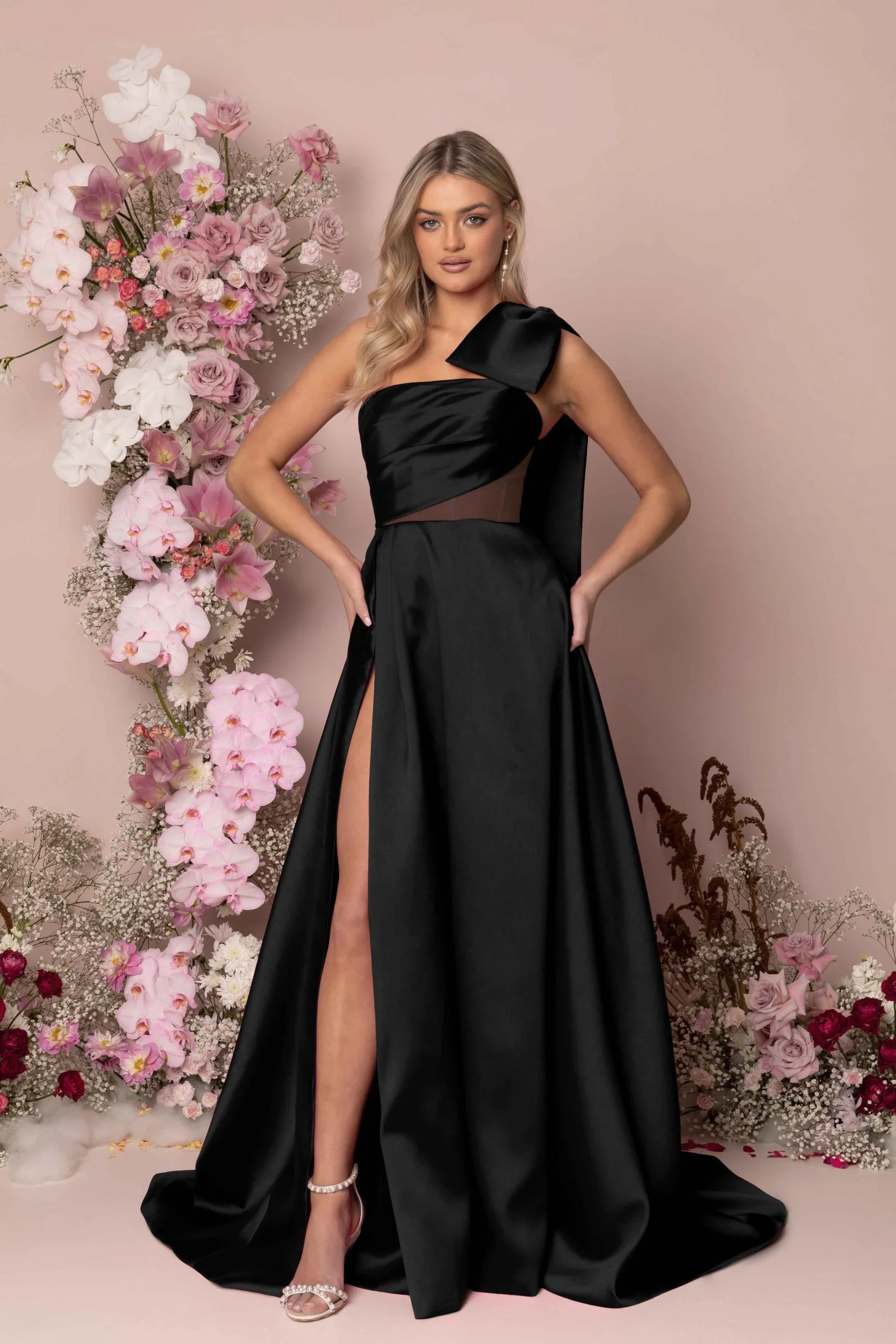 Madi Lane Kinsley A-line wedding dress with an illusion bodice, asymmetrical pleat detailing, a detachable one-shoulder oversized bow, and a dramatic leg split.