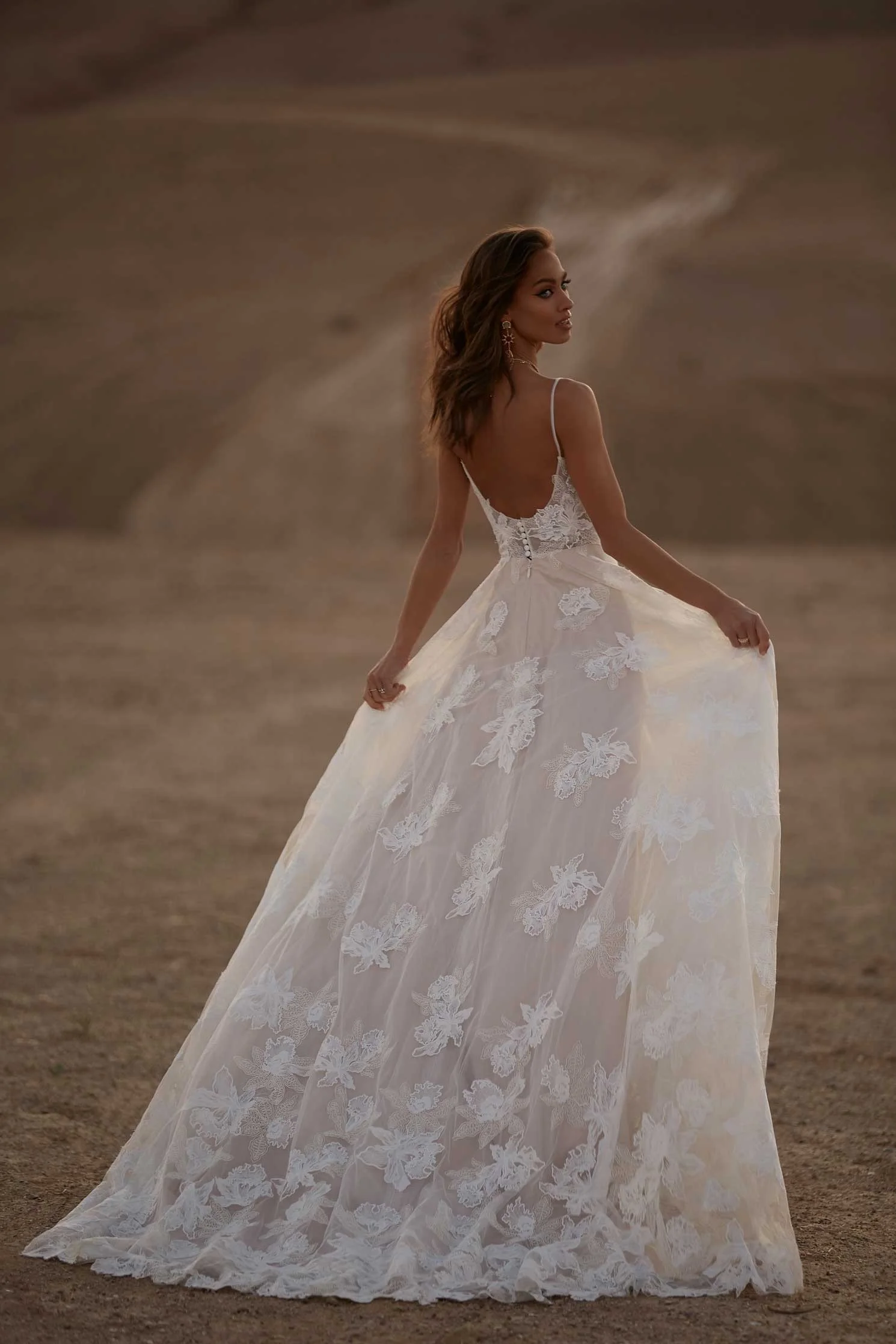 Madi Lane Avery A-line wedding dress with thin spaghetti straps, large floral lace appliqué, and a shimmering glitter tulle under-layer finished with a low circular back and pearl buttons