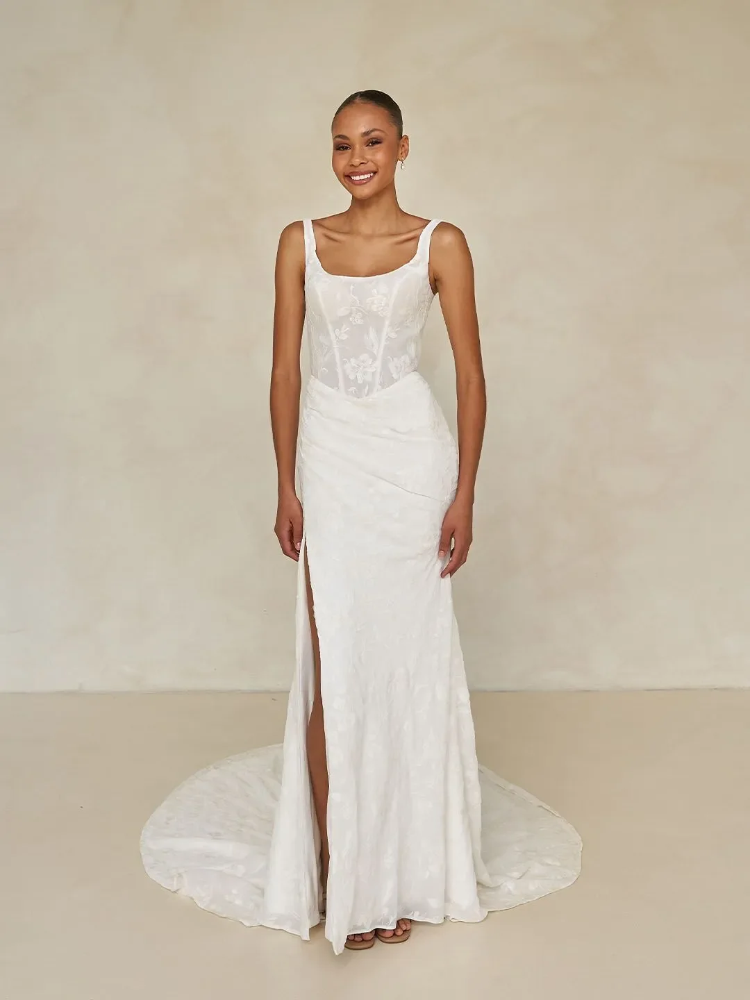 Madi Lane Wilcox minimalist fit-and-flare wedding dress with a scoop illusion bodice, embroidered tulle chiffon, Basque waist, asymmetrical draping, and leg split.