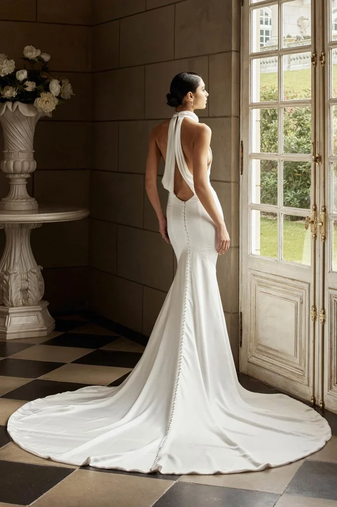 Shop Tokyo by Jeune at Bride To Be Couture in Sacramento, California. This minimalist fitted wedding dress features a high halter neckline, open-back design, and sleek modern bridal silhouette