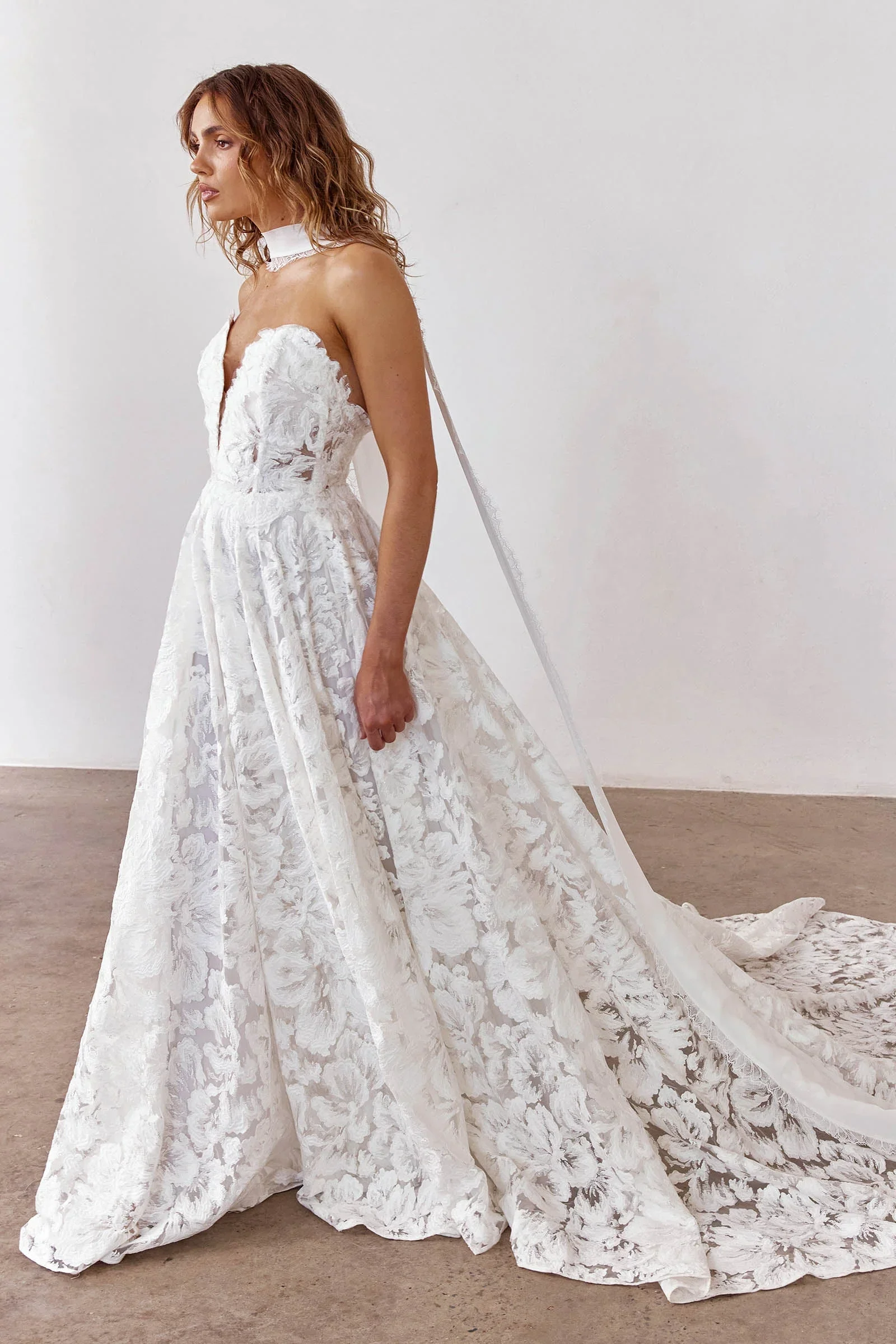 Strapless sweetheart A-line gown in dimensional floral embroidered lace with a hand-moulded appliqué bodice and voluminous layered skirt.