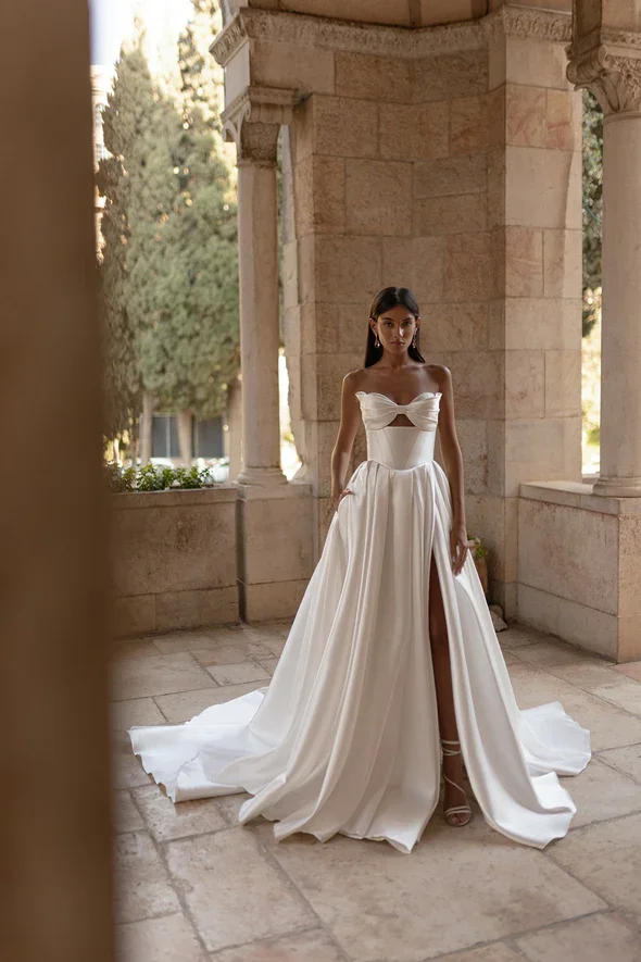 Julie Vino Vita Mikado A-line wedding gown with a strapless sweetheart neckline, Basque waistline, considered cutouts, leg slit, and statement bow.