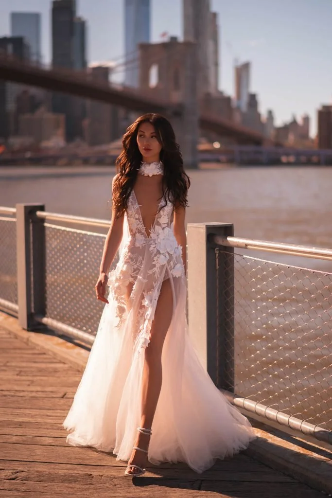 Oksana by Muse by Berta is a couture floral lace wedding gown featuring a plunging illusion neckline, sheer bodice, high slit, and soft tulle skirt for the modern romantic bride.