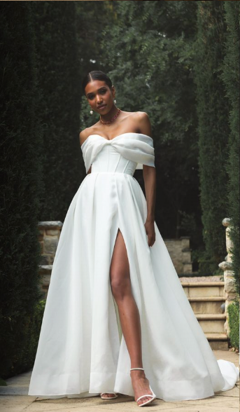 Madi Lane Prestyn A-line wedding gown in layered organza with softly pleated off-the-shoulder straps, a bow-inspired bodice, leg split, and cathedral-length train.