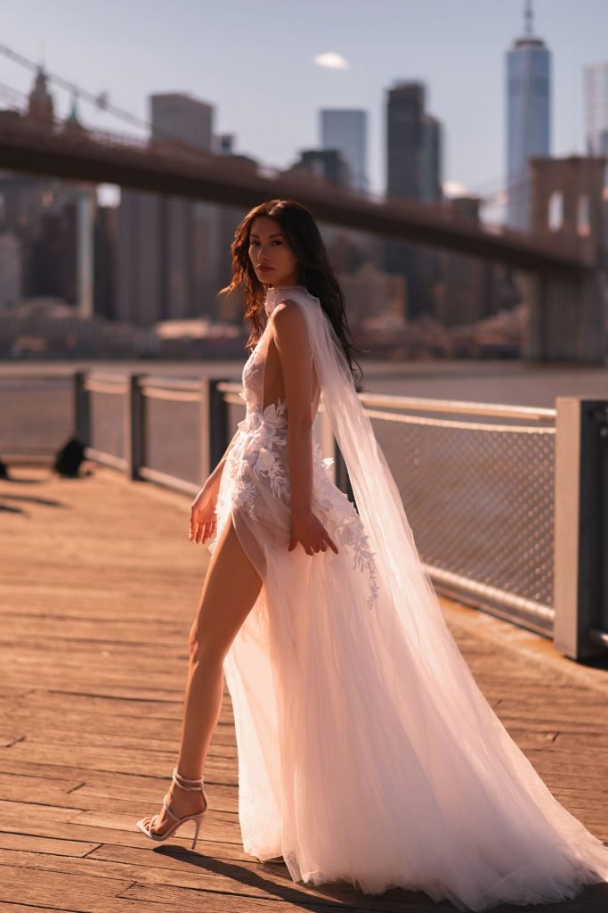 Oksana by Muse by Berta is a couture floral lace wedding gown featuring a plunging illusion neckline, sheer bodice, high slit, and soft tulle skirt for the modern romantic bride.