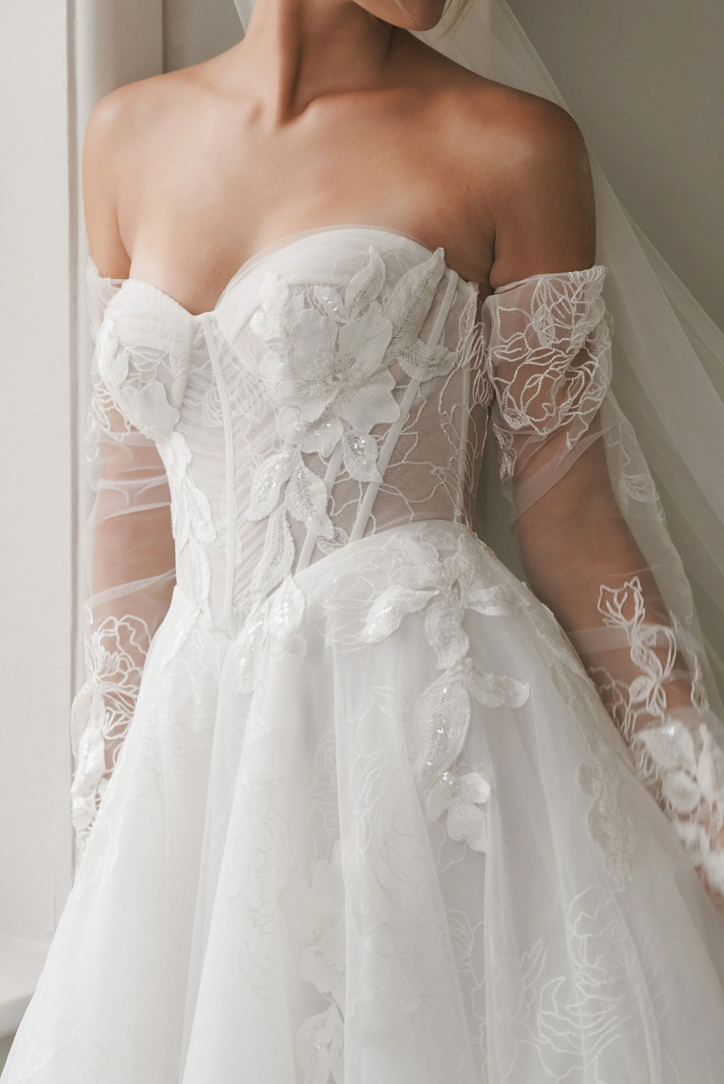 La Premiere Athena beaded floral lace A-line wedding gown with strategic blank spaces, pleated bodice, detachable sleeves, and veil.