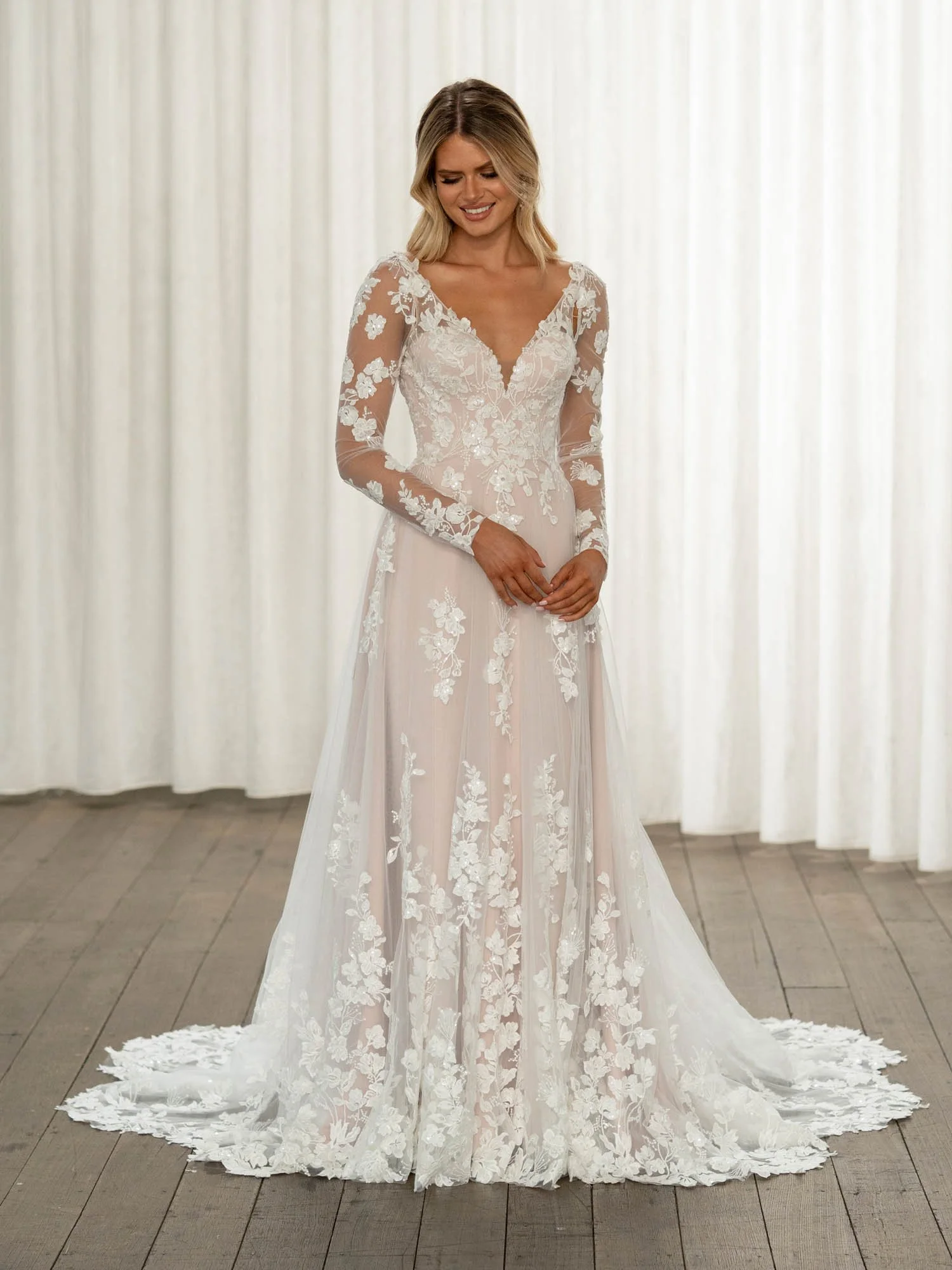 Madi Lane Tucker A-line wedding dress with a higher V-neckline, organic sequin floral lace, detachable long lace sleeves, and a scalloped semi-illusion train.
