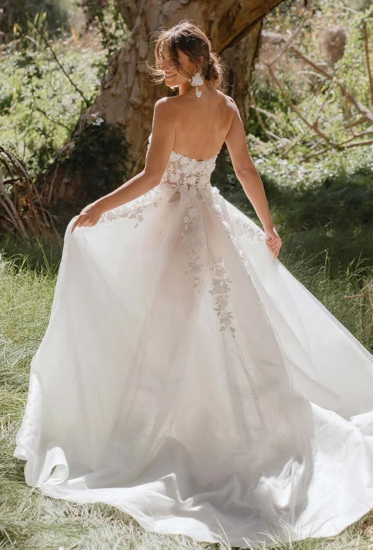 Madi Lane Samara strapless A-line wedding gown with an illusion bodice, 3D floral lace, dramatic tulle skirt, and detachable long-sleeve illusion topper.