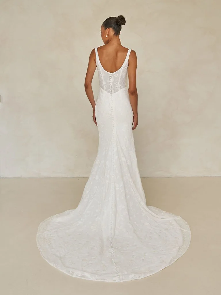 Madi Lane Wilcox minimalist fit-and-flare wedding dress with a scoop illusion bodice, embroidered tulle chiffon, Basque waist, asymmetrical draping, and leg split.