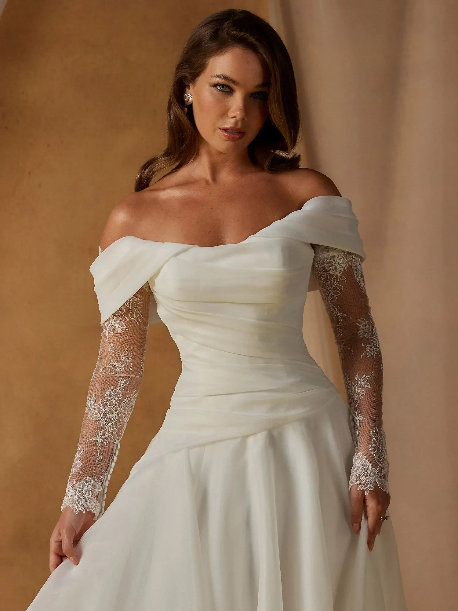 Madi Lane Nettle A-line organza wedding dress with three styling options — strapless, off-shoulder sleeves, or lace illusion sleeves — plus drop-waist pleating and pearl-trimmed train.