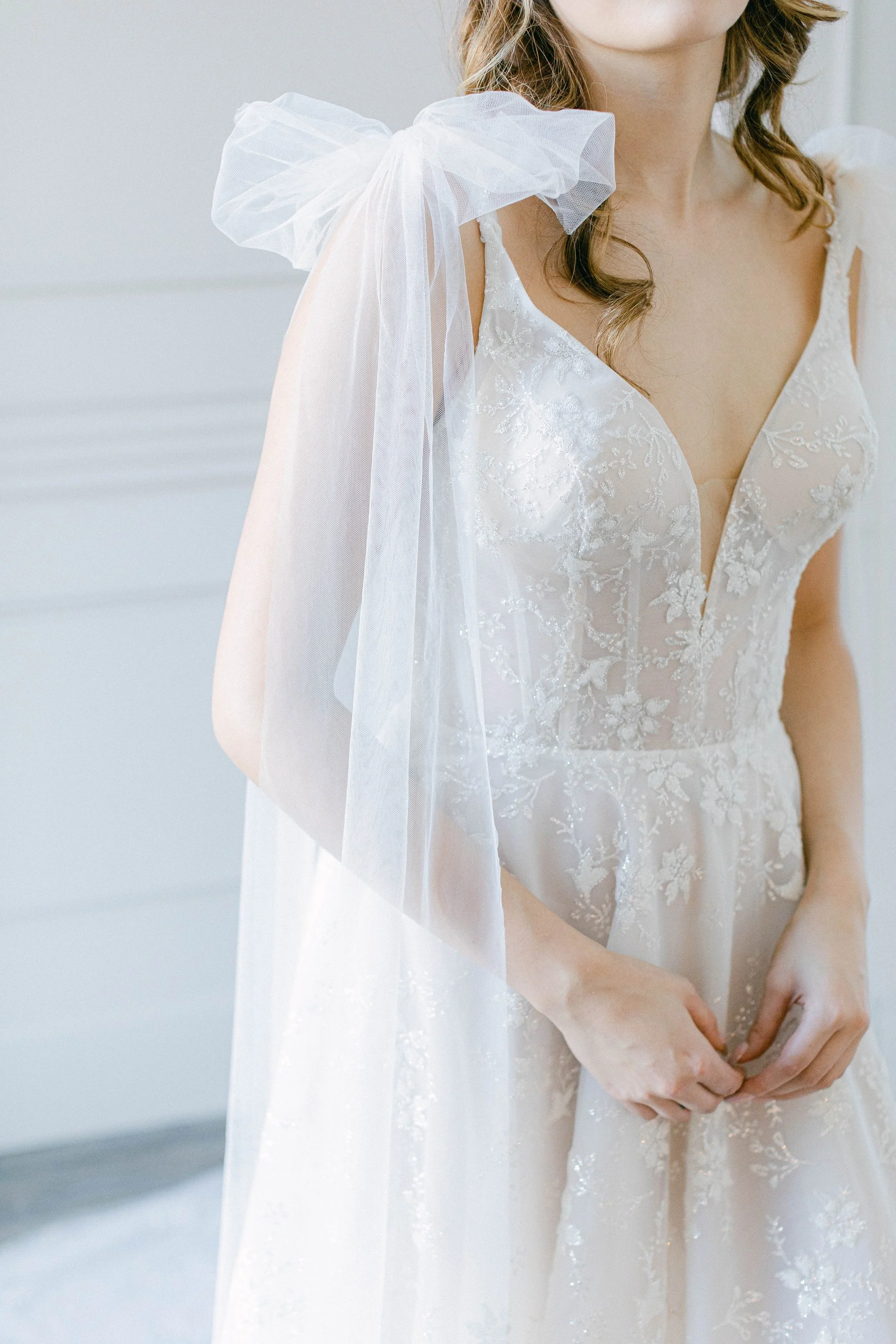 Elizabeth Lee Mia light Israeli lace A-line wedding dress with deep V plunge neckline and detachable bows.