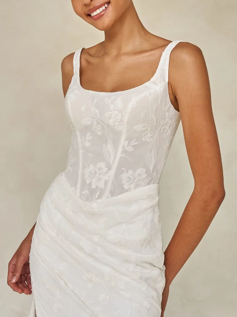 Madi Lane Wilcox minimalist fit-and-flare wedding dress with a scoop illusion bodice, embroidered tulle chiffon, Basque waist, asymmetrical draping, and leg split.
