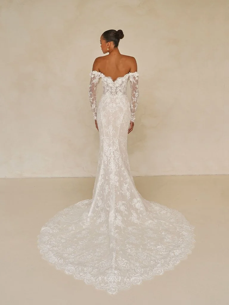 Madi Lane Wade fit-and-flare Chantilly lace wedding gown with a front-plunge bodice, 3D floral appliqués, vertical seam contouring, and detachable off-the-shoulder sleeves.