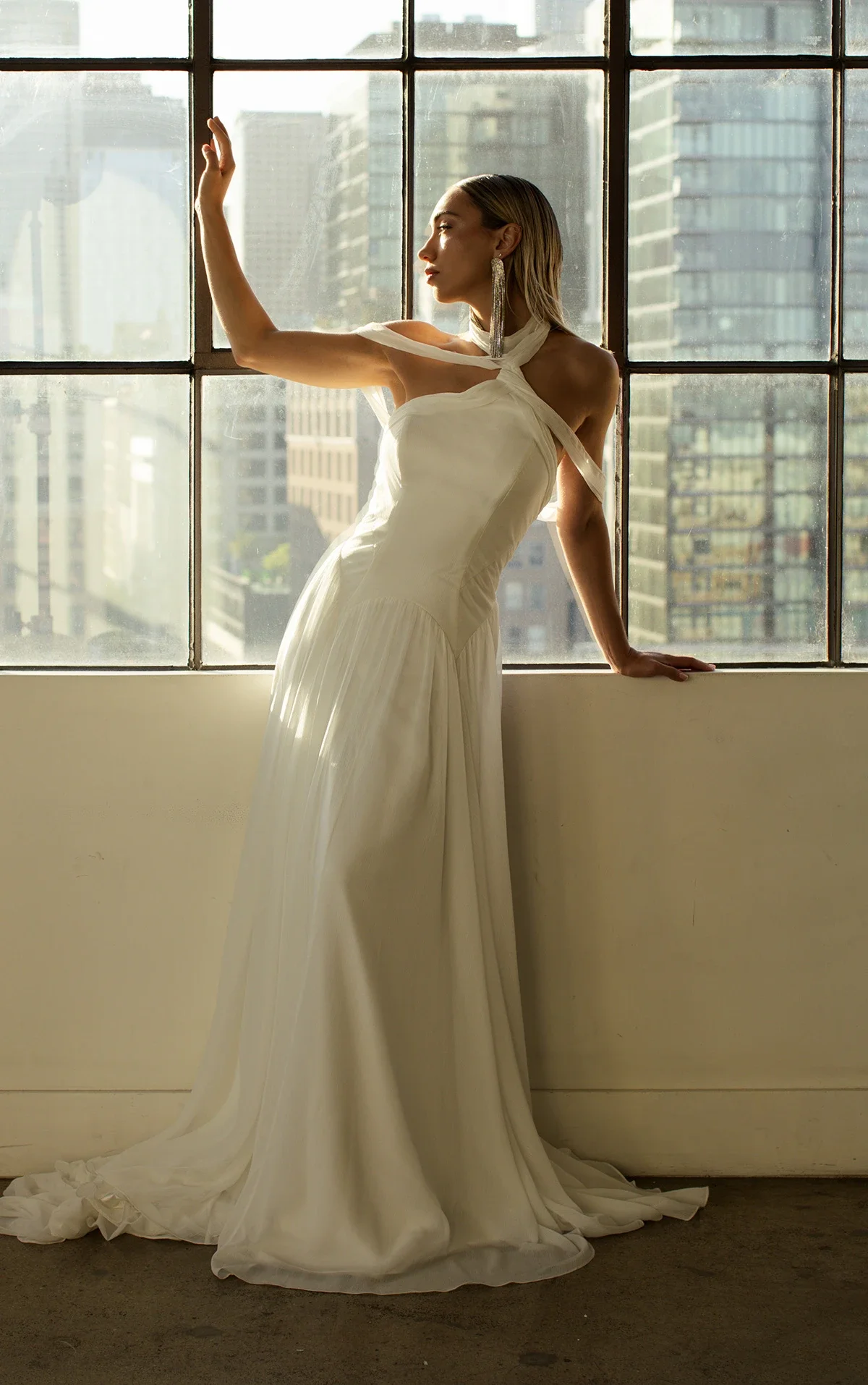 All Who Wander Falon off-the-shoulder crinkle chiffon A-line wedding dress with asymmetrical high neckline, drop seams, and flowing breezy skirt, available at Bride To Be Couture in Sacramento.