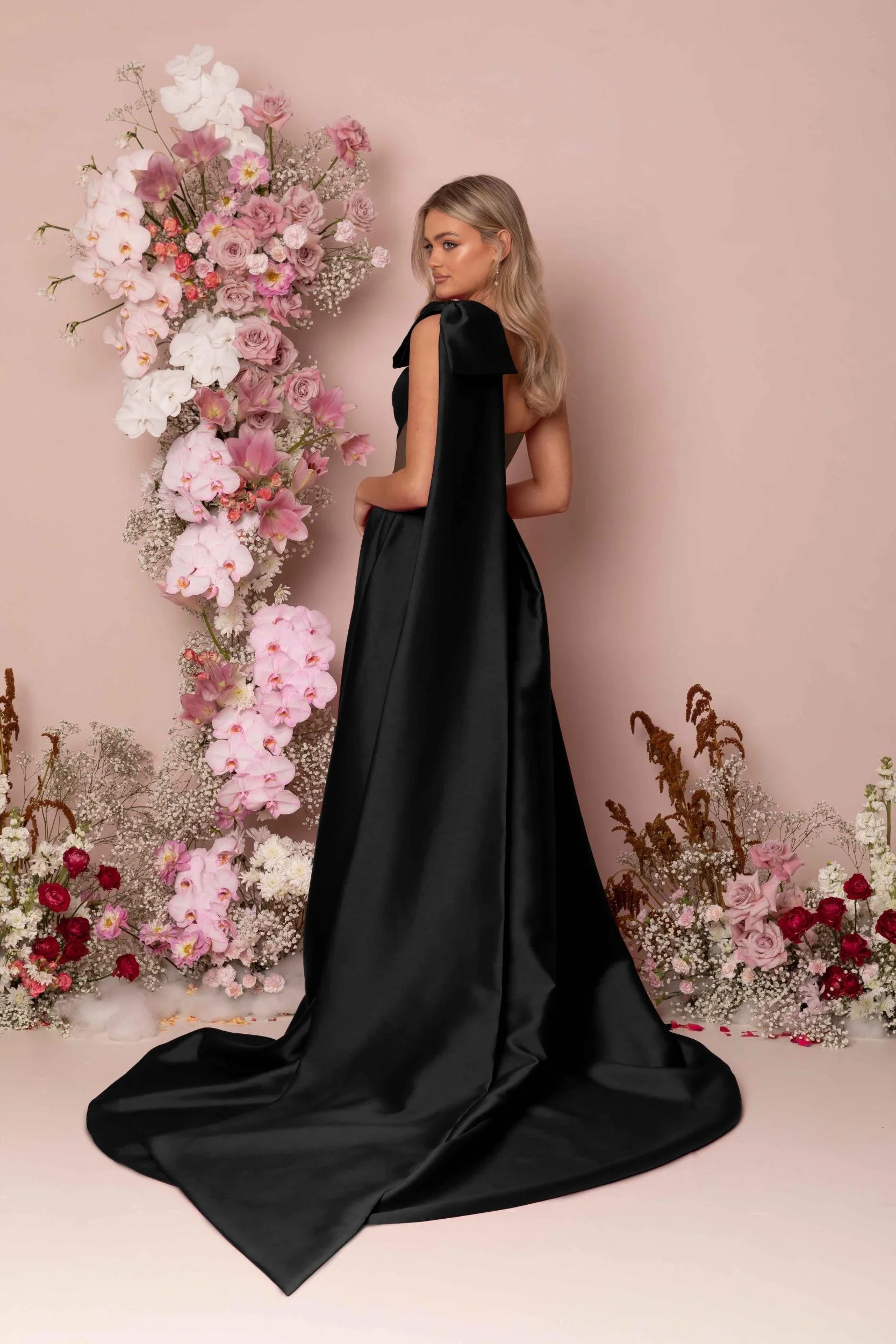 Madi Lane Kinsley A-line wedding dress with an illusion bodice, asymmetrical pleat detailing, a detachable one-shoulder oversized bow, and a dramatic leg split.