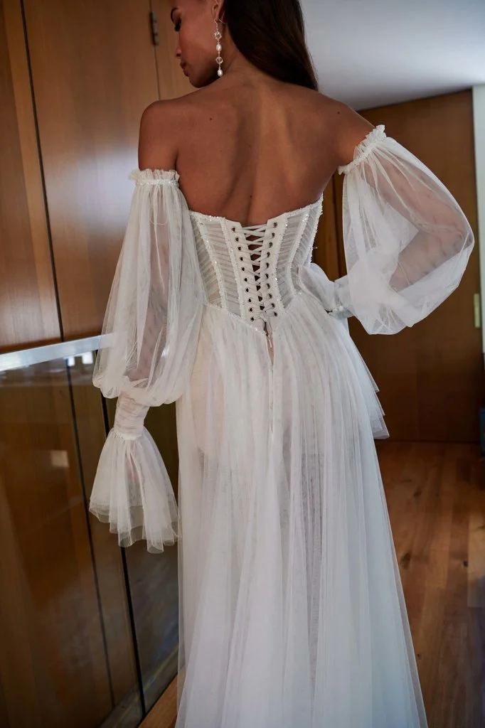 Serene Ame Kinney A-line tulle wedding dress with sweetheart illusion bustier bodice, beaded trim, side slit with jersey shorts lining, and detachable off-shoulder sleeves.
