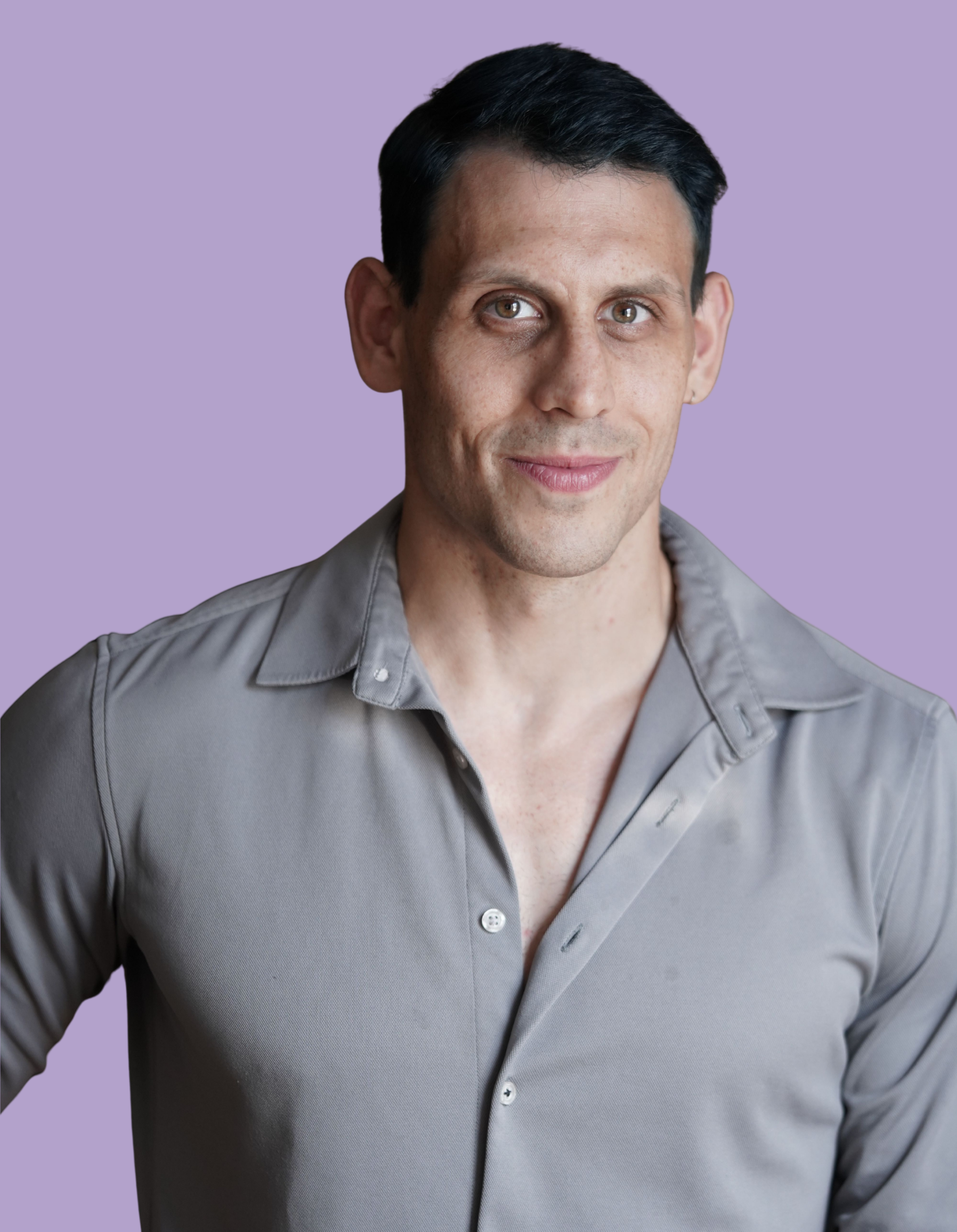Close-up of a man with short dark hair and light skin wearing a gray button-up shirt with an open collar against a solid purple background.