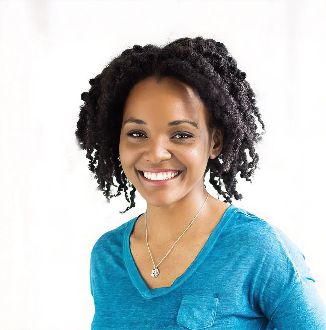 A woman with natural curly hair, smiling, wearing a blue shirt and a silver necklace with a pendant.