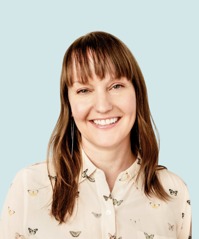 A woman with shoulder-length brown hair and bangs, smiling, wearing a cream blouse with butterfly prints, against a light blue background.