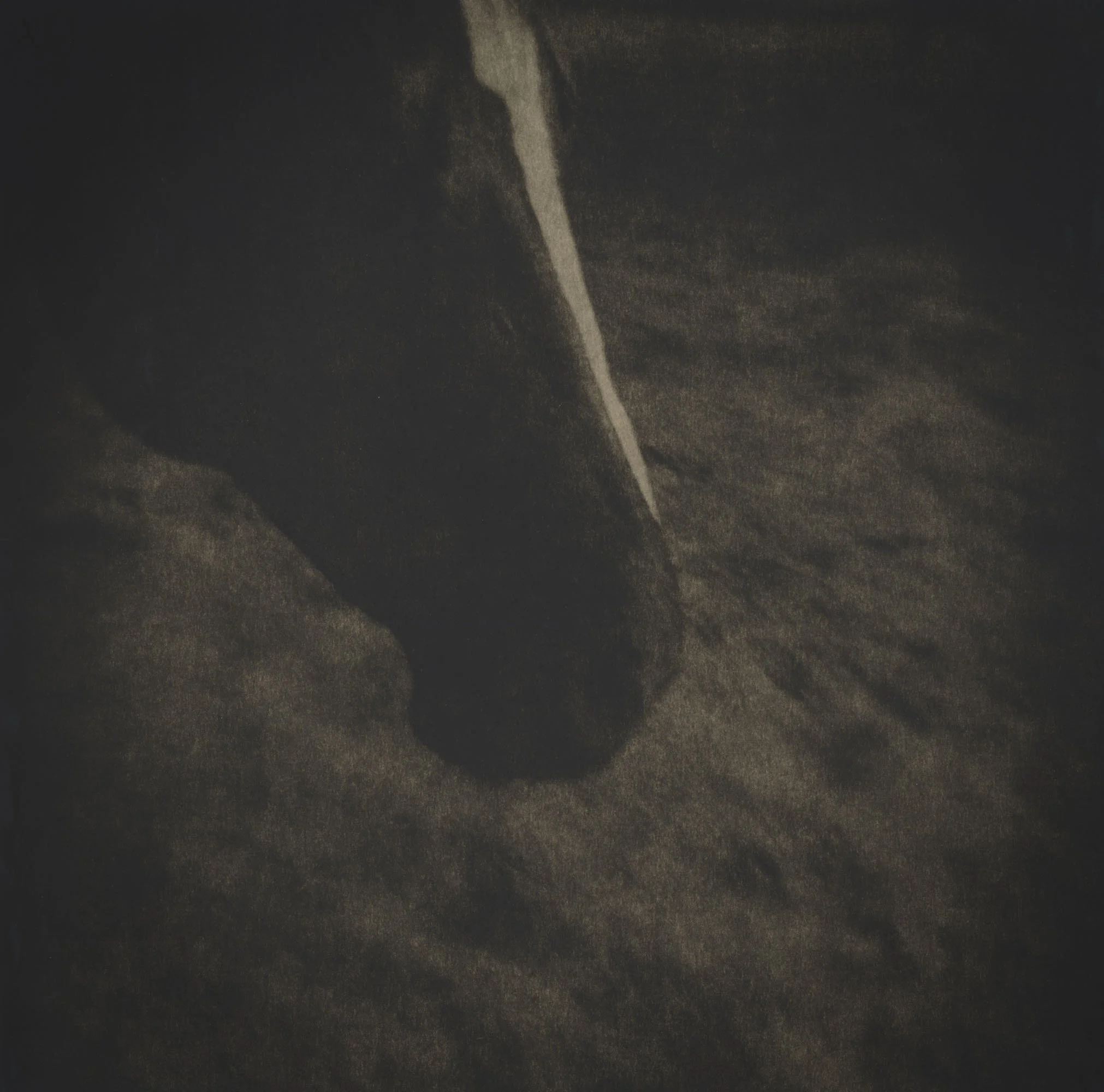 A close-up of a person's foot wearing a dark shoe, stepping onto a sandy surface at night.